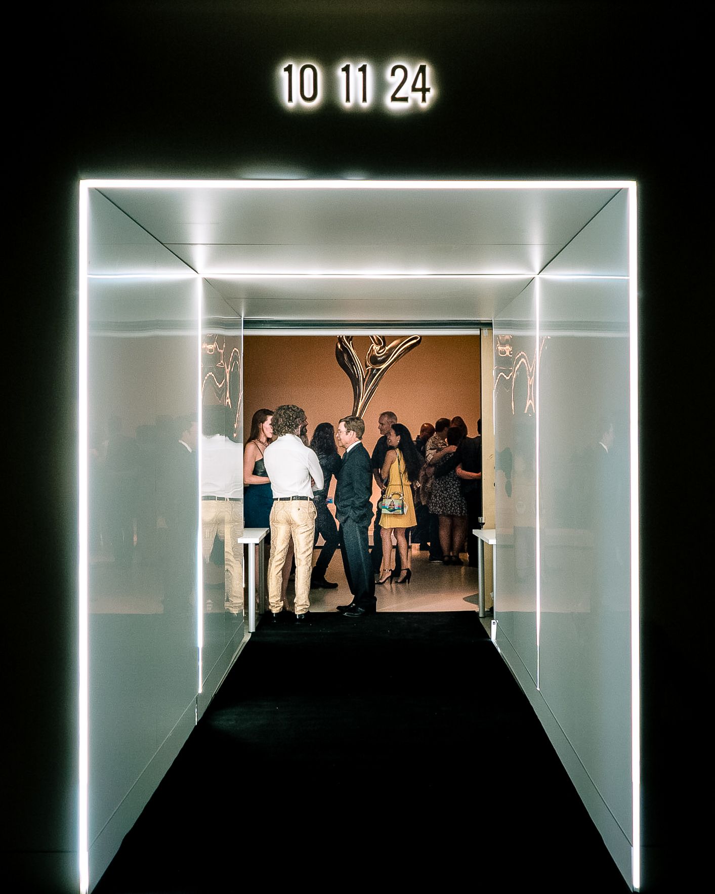 A backlit modern corridor with LED lighting and a group of people gathered at the end displays '10 11 24' at the top.