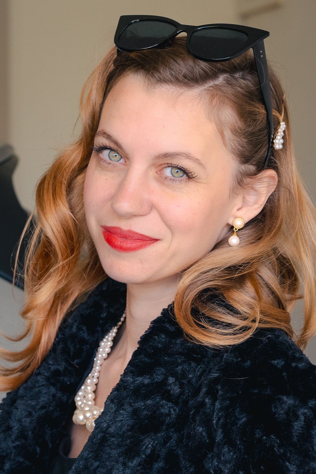 Portrait featuring vintage-styled glamour with sunglasses and pearl accessories against neutral background.