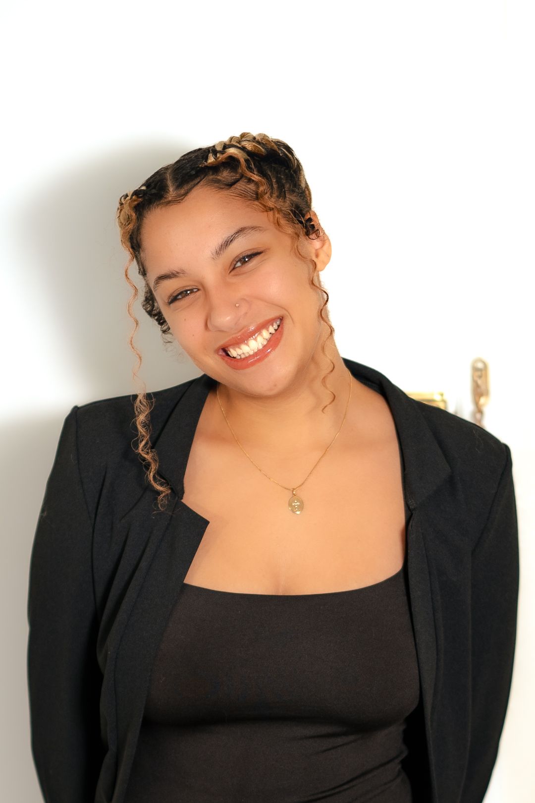Professional headshot of someone in a black blazer with curly hair and bright smile against white background.