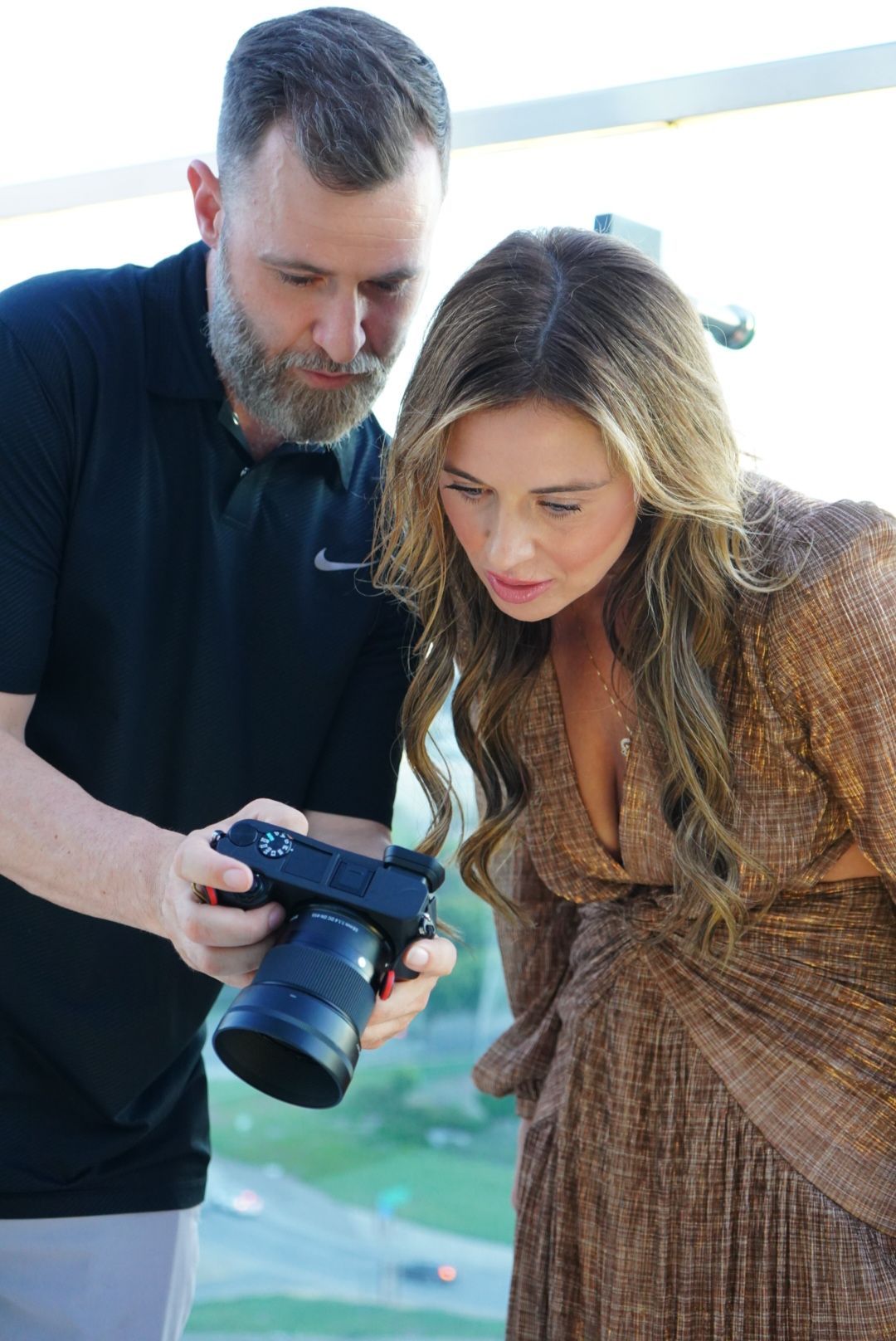 Two people reviewing photos on a camera display outdoors in natural lighting.