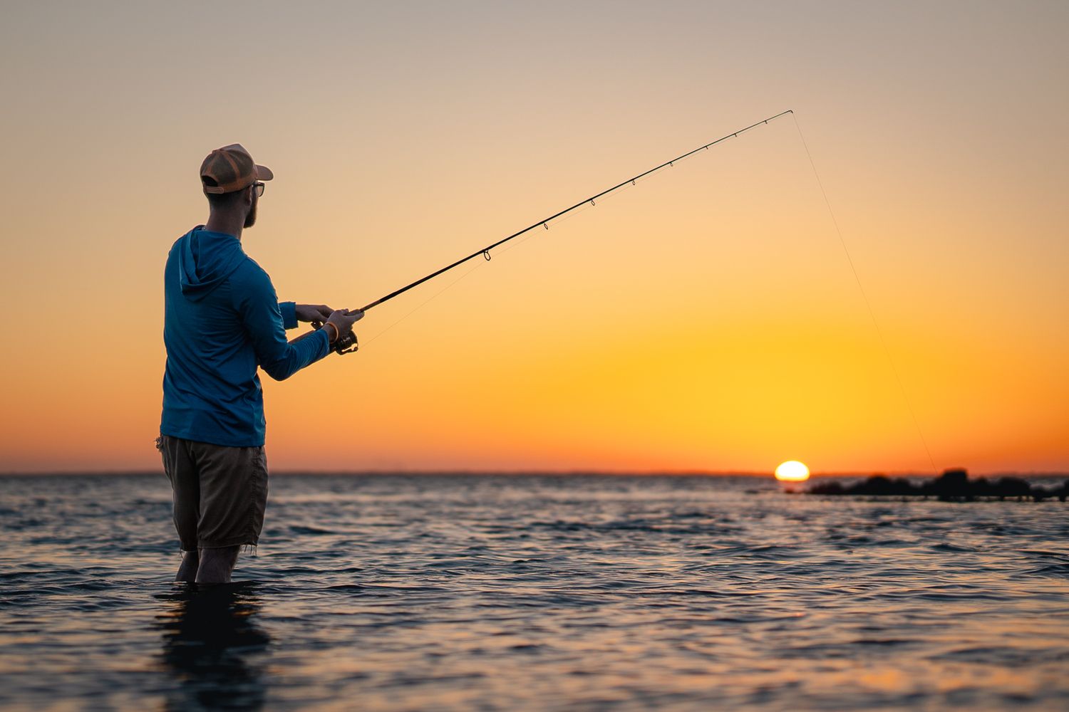 Silhouette of person fishing in ocean water during golden sunset.