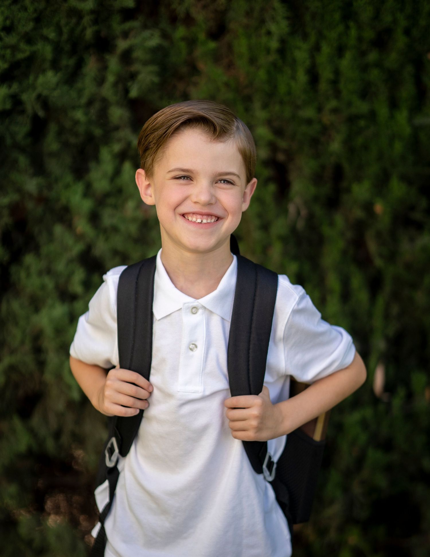 Young student wearing white polo shirt and backpack smiling outdoors.