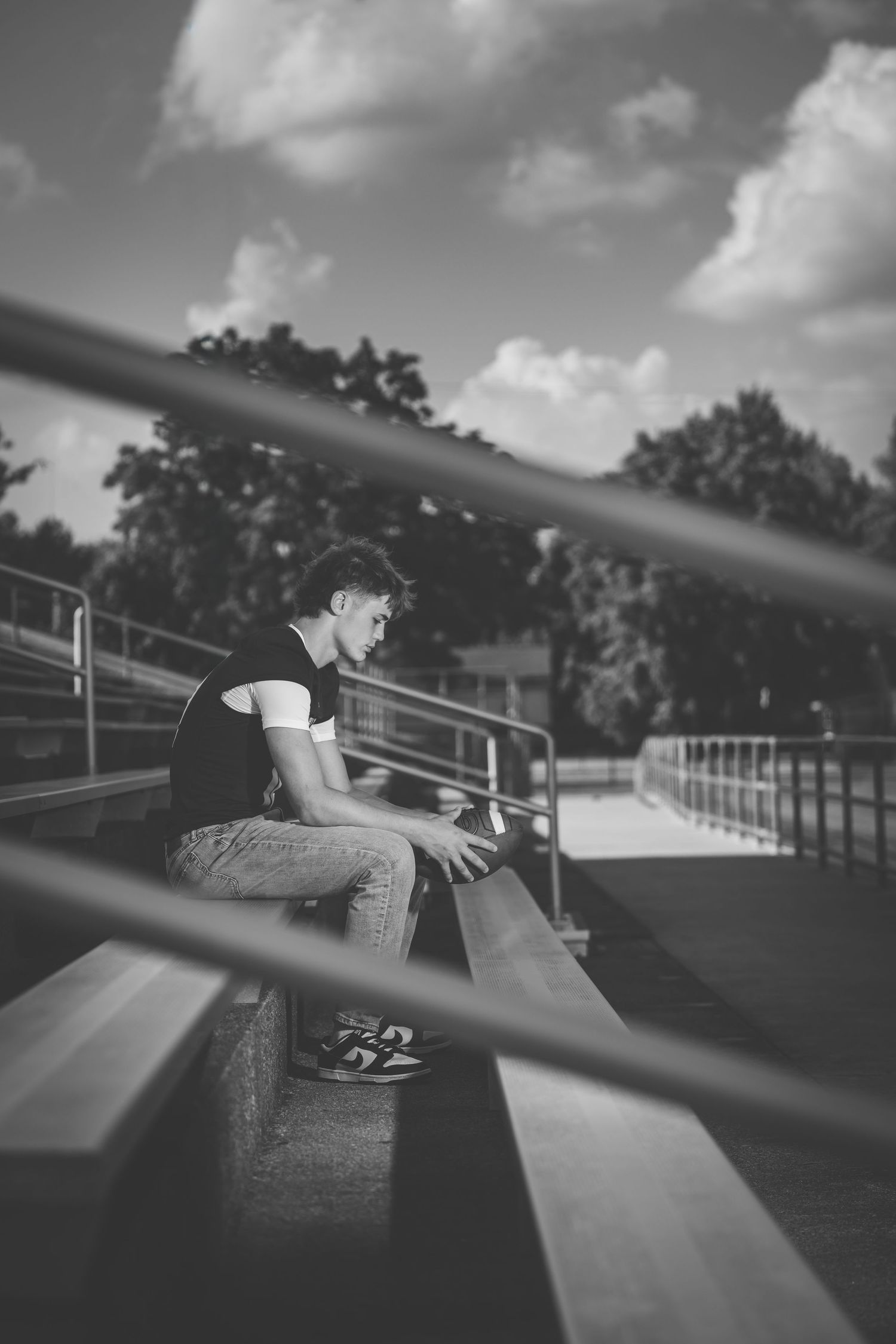 A person sits alone on empty bleachers at a sports field, captured in dramatic black and white photography.