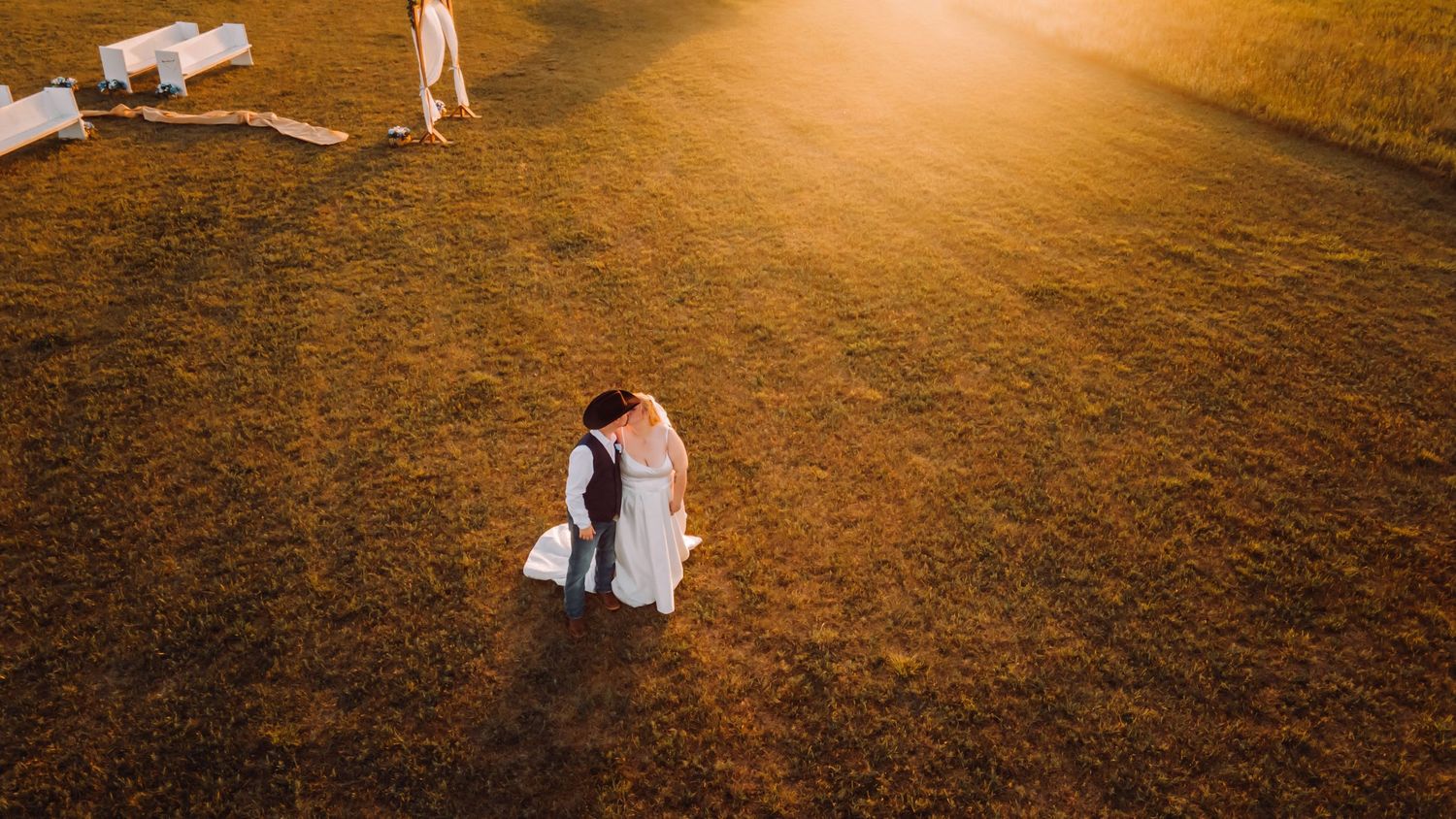 Aerial drone view of a couple embracing on brown grass field at golden sunset.