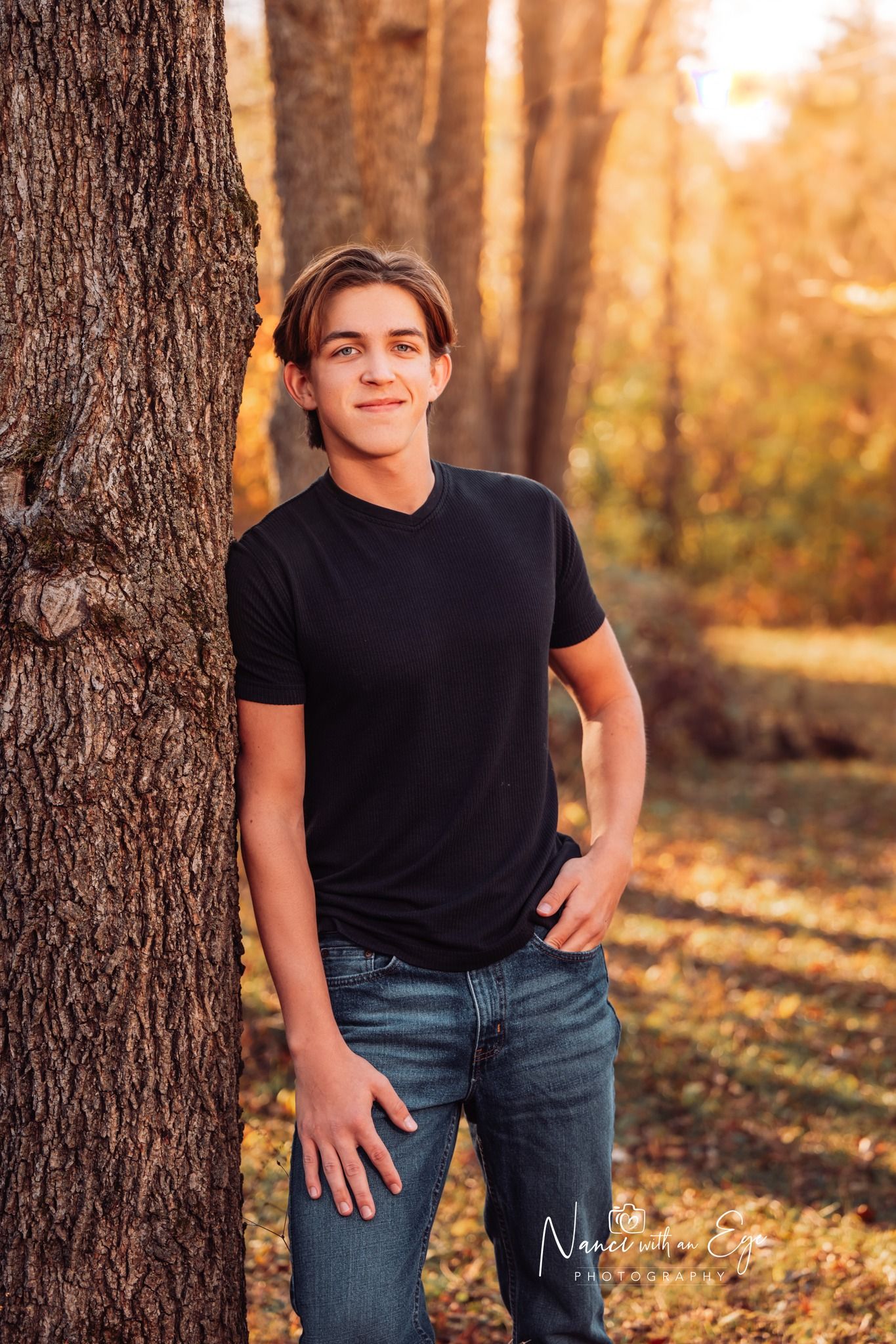 senior photo of boy in black shirt leaning against a tree in fall autumn