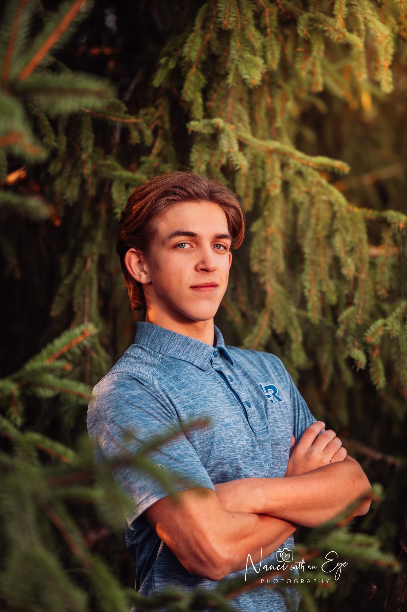 senior photo of boy in blue shirt leaning against a tree in fall autumn