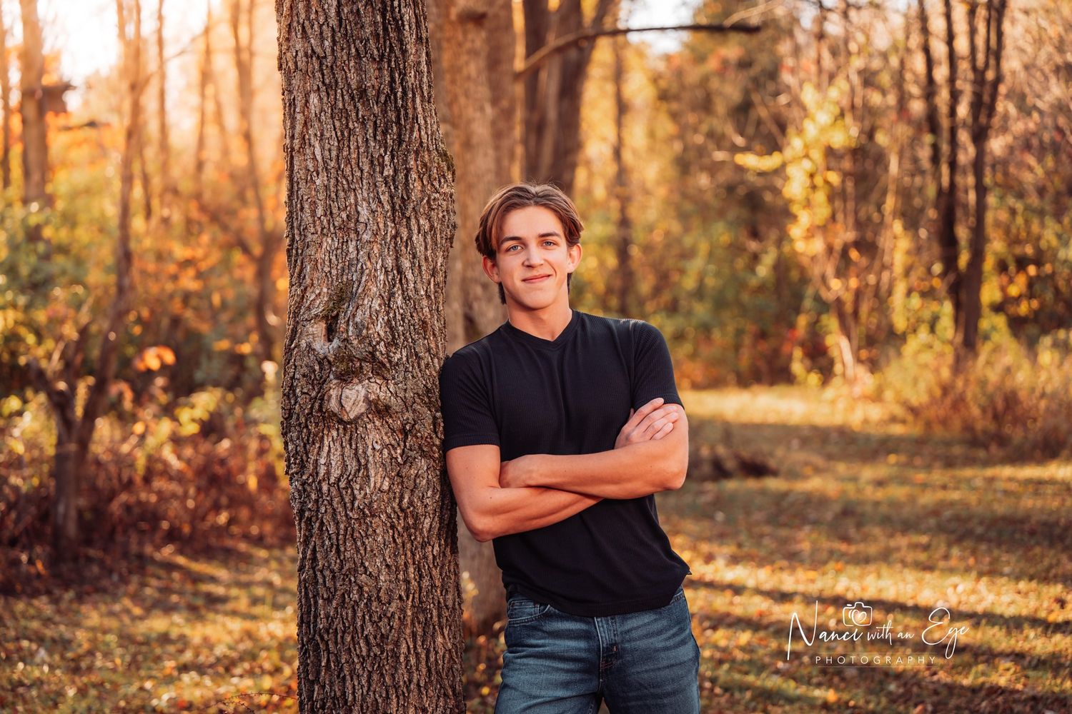 senior photo of boy in black shirt leaning against a tree in fall autumn