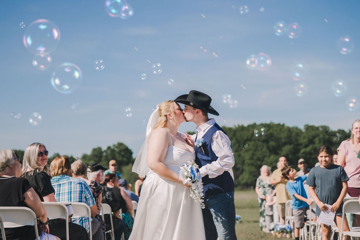 Bubbles float through the air as wedding guests celebrate during an outdoor countryside ceremony by the mountains.