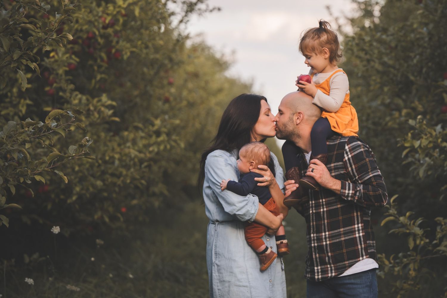 family of four photoshoot in the fall kissing in the orchard