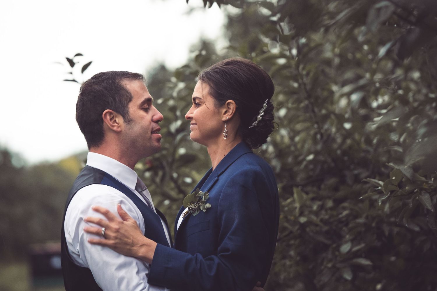 close up of bride and groom in orchard bride wearing grooms jacket coat