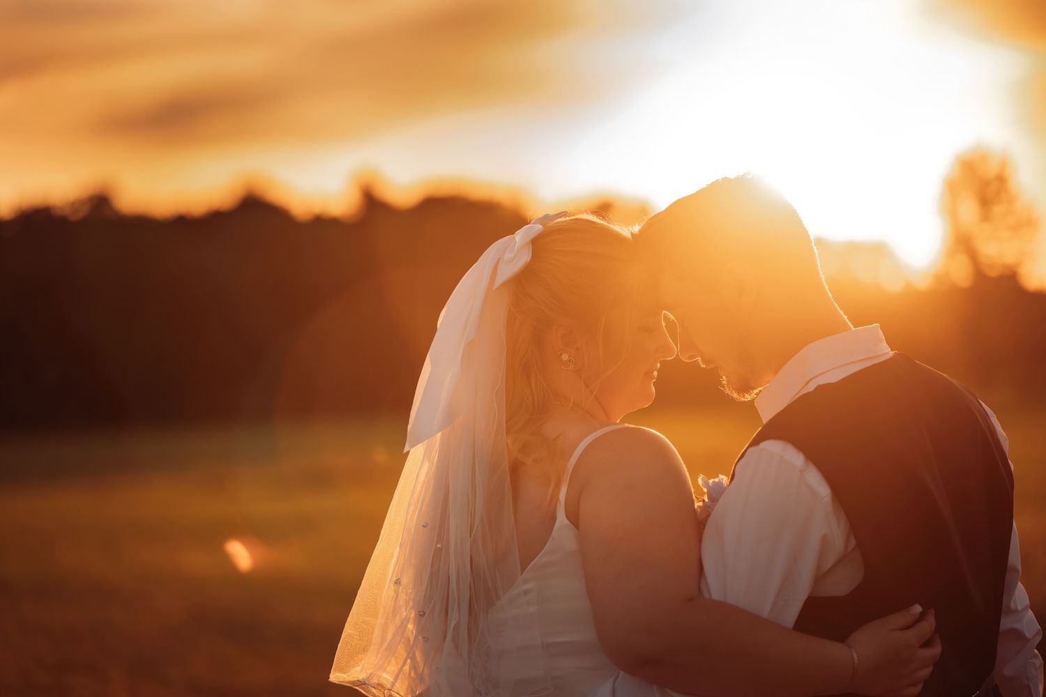 A romantic sunset silhouette of newlyweds embracing outdoors with a glowing golden sky in the background.