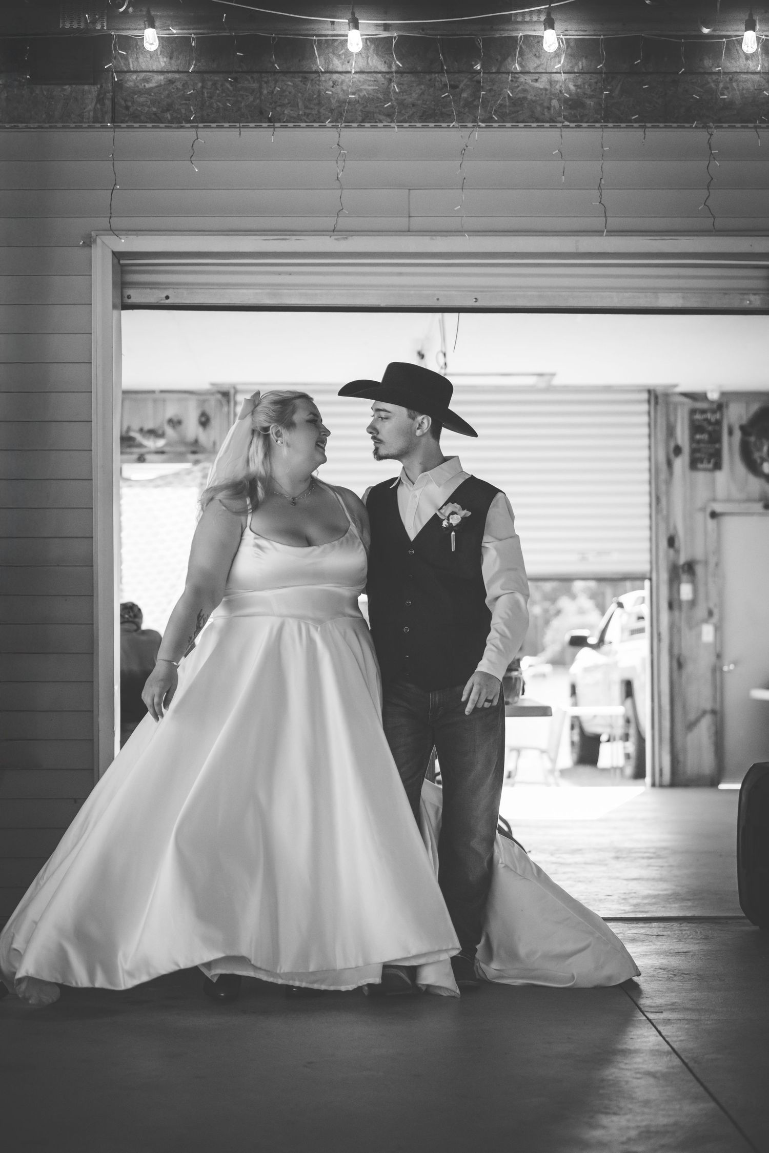 A black and white wedding photo shows a couple in western-inspired attire sharing an intimate moment in a rustic venue.
