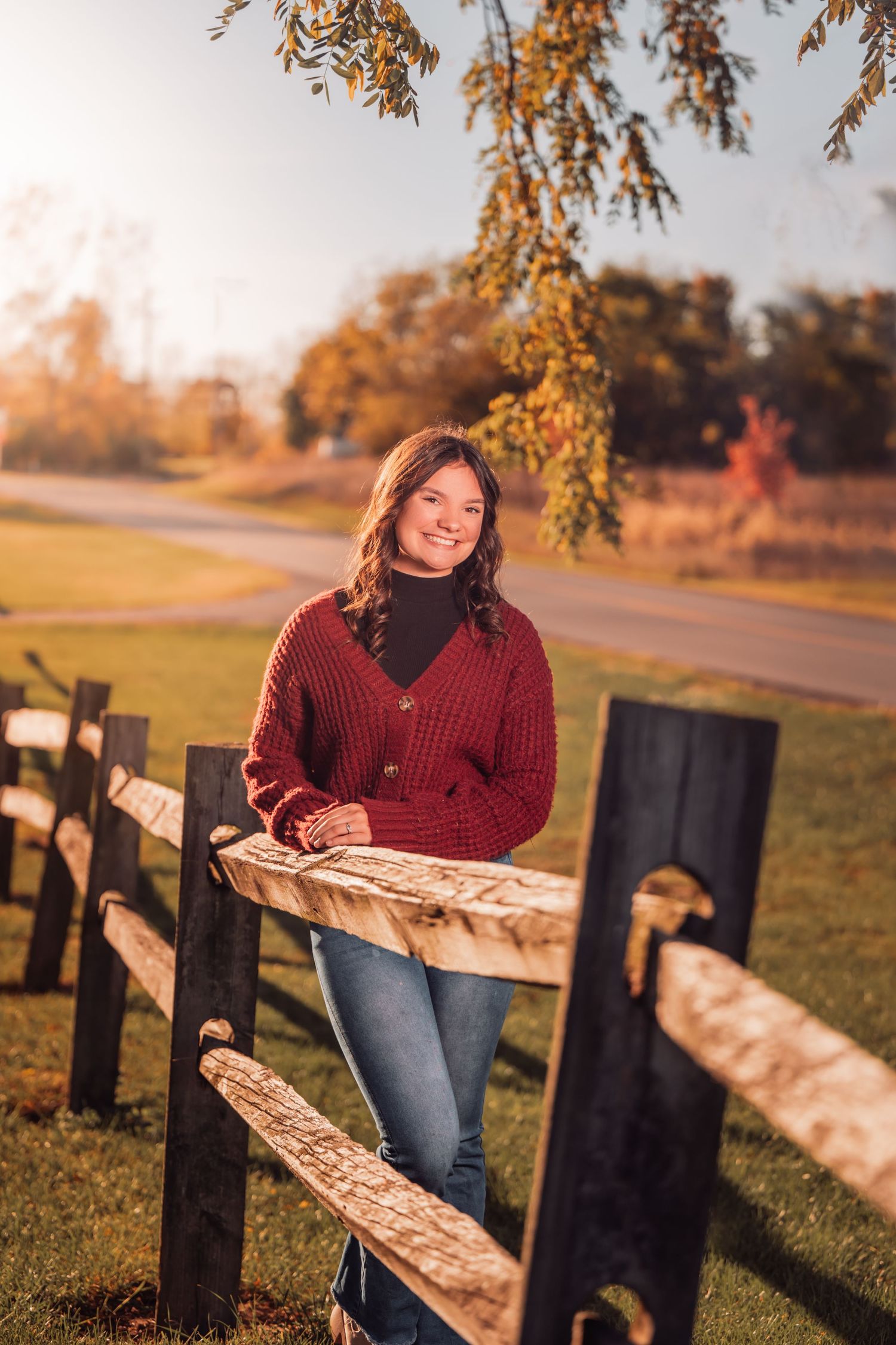 senior photo in fall of girl leaning against a wooden fence