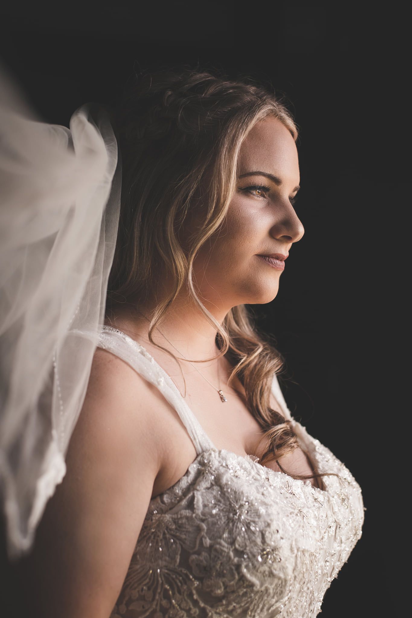 beautiful bride looking out window, black background, natural light