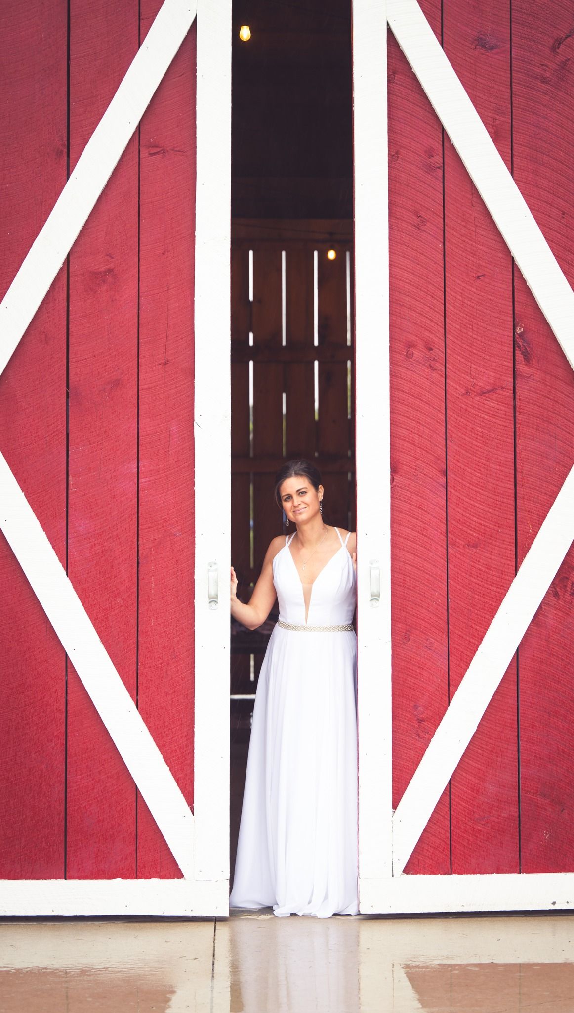 bride peaking through red barn doors on wedding day