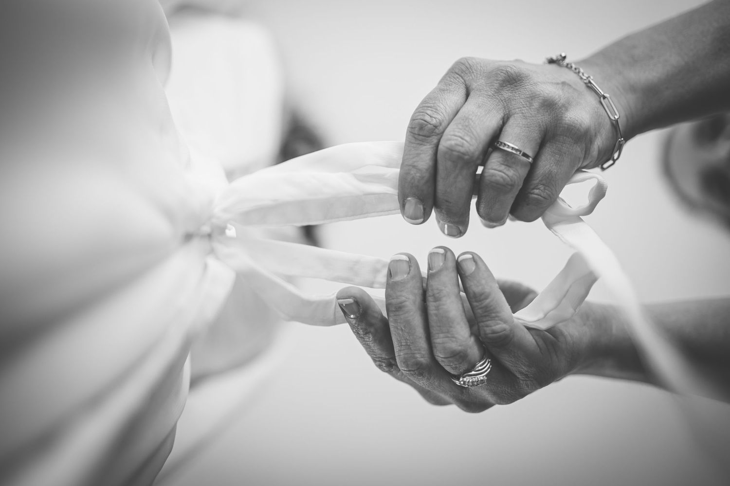 A pair of hands carefully exchanging a white delicate object in an ethereal black and white photograph.