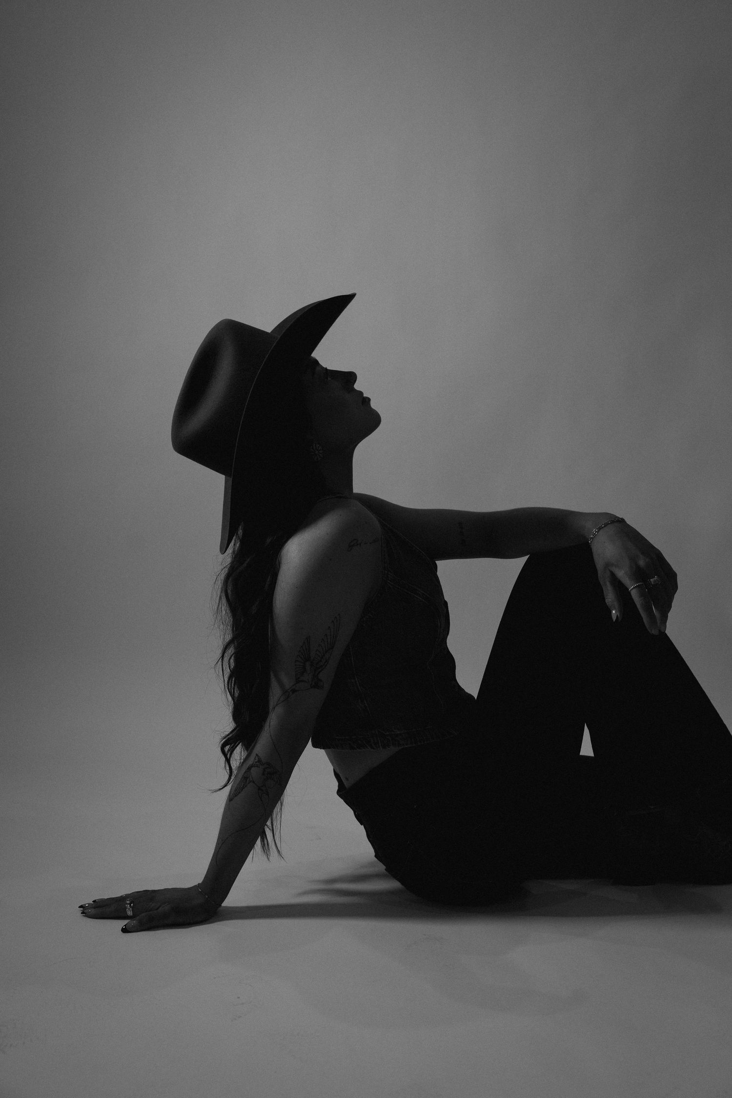 Silhouette of a woman in a wide-brim hat sitting on the floor in black and white.