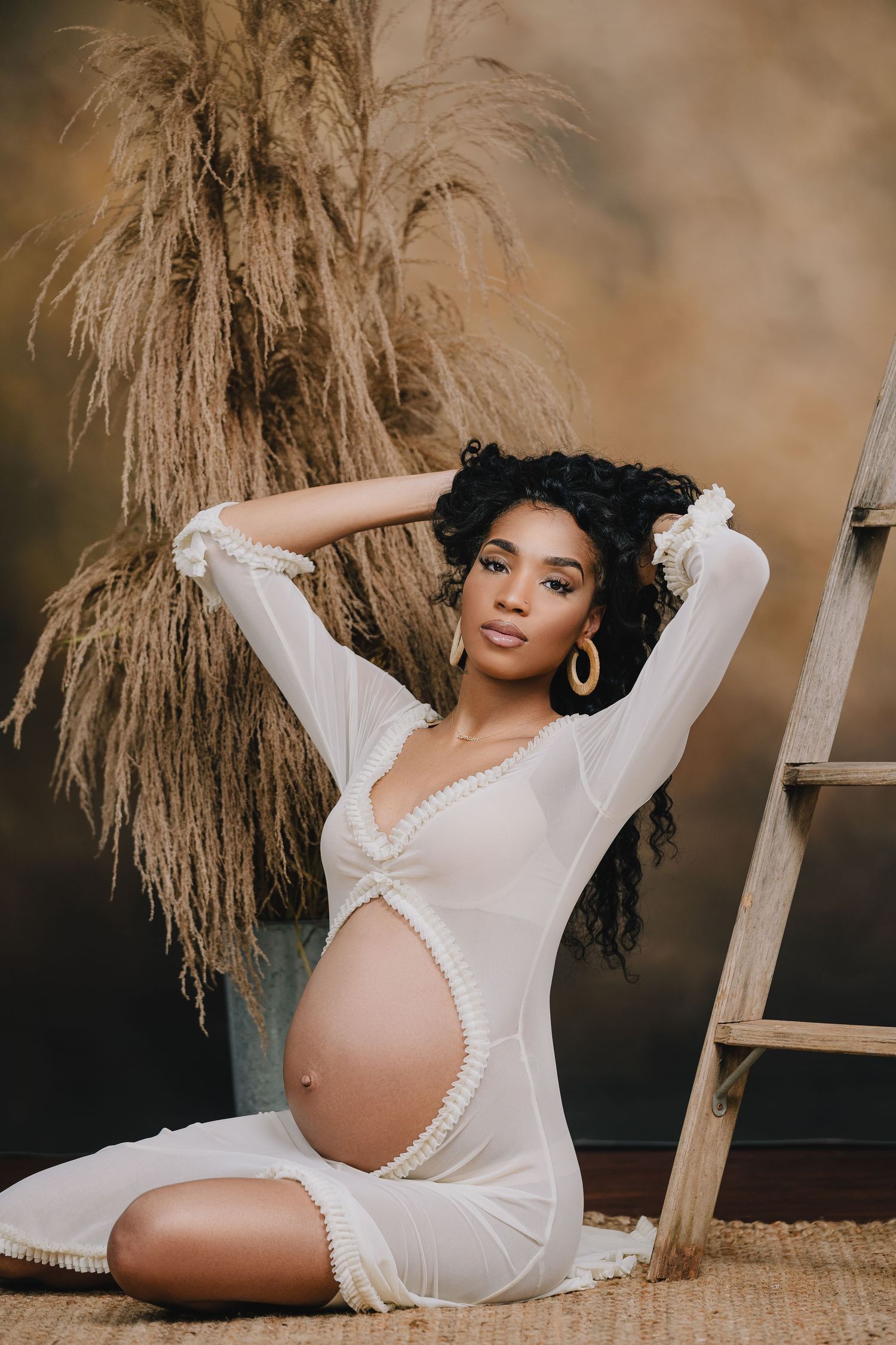Maternity photoshoot featuring white lace lingerie and dried pampas grass decor.