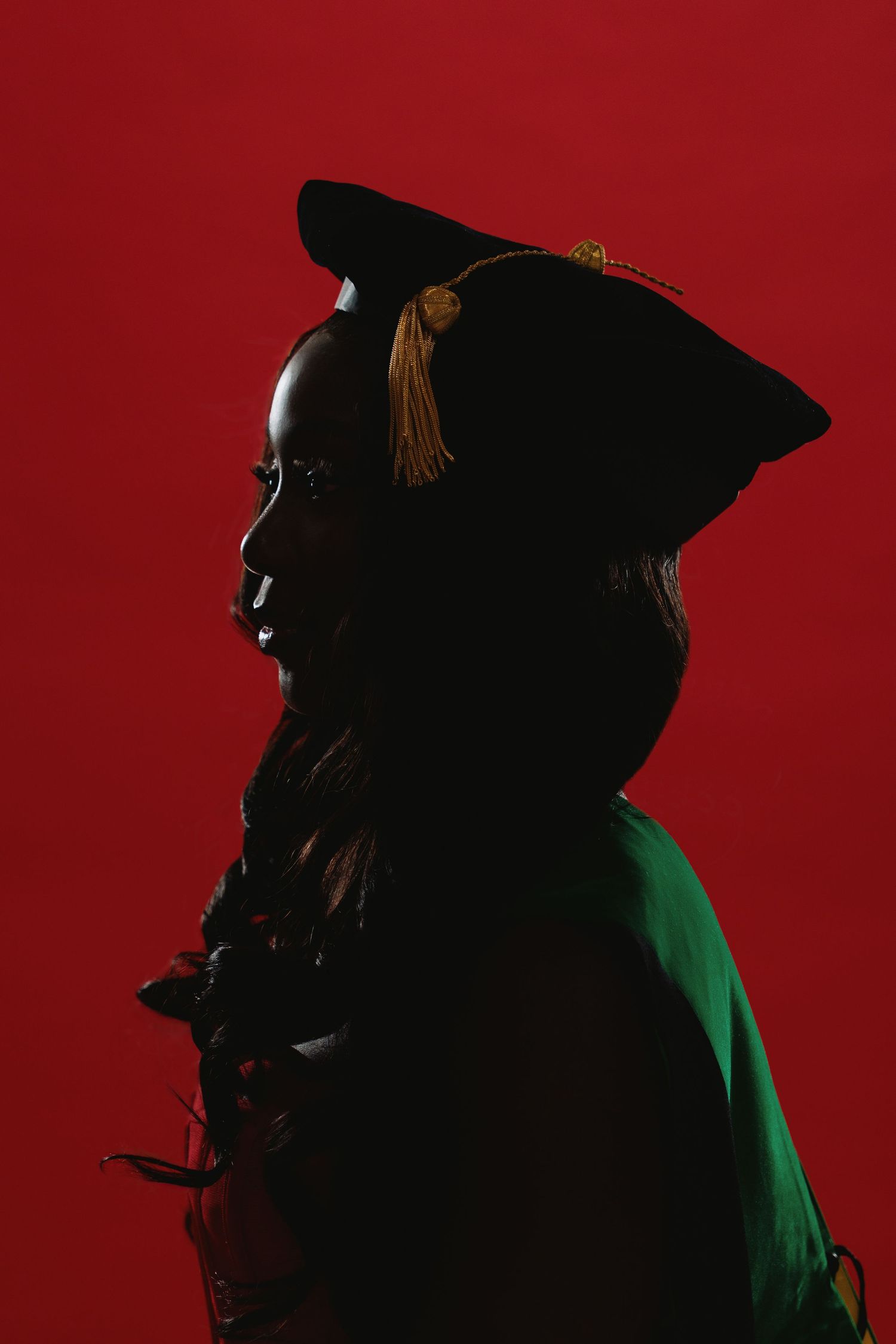A silhouetted figure wearing a graduation cap stands against a dramatic red background with green accent lighting.