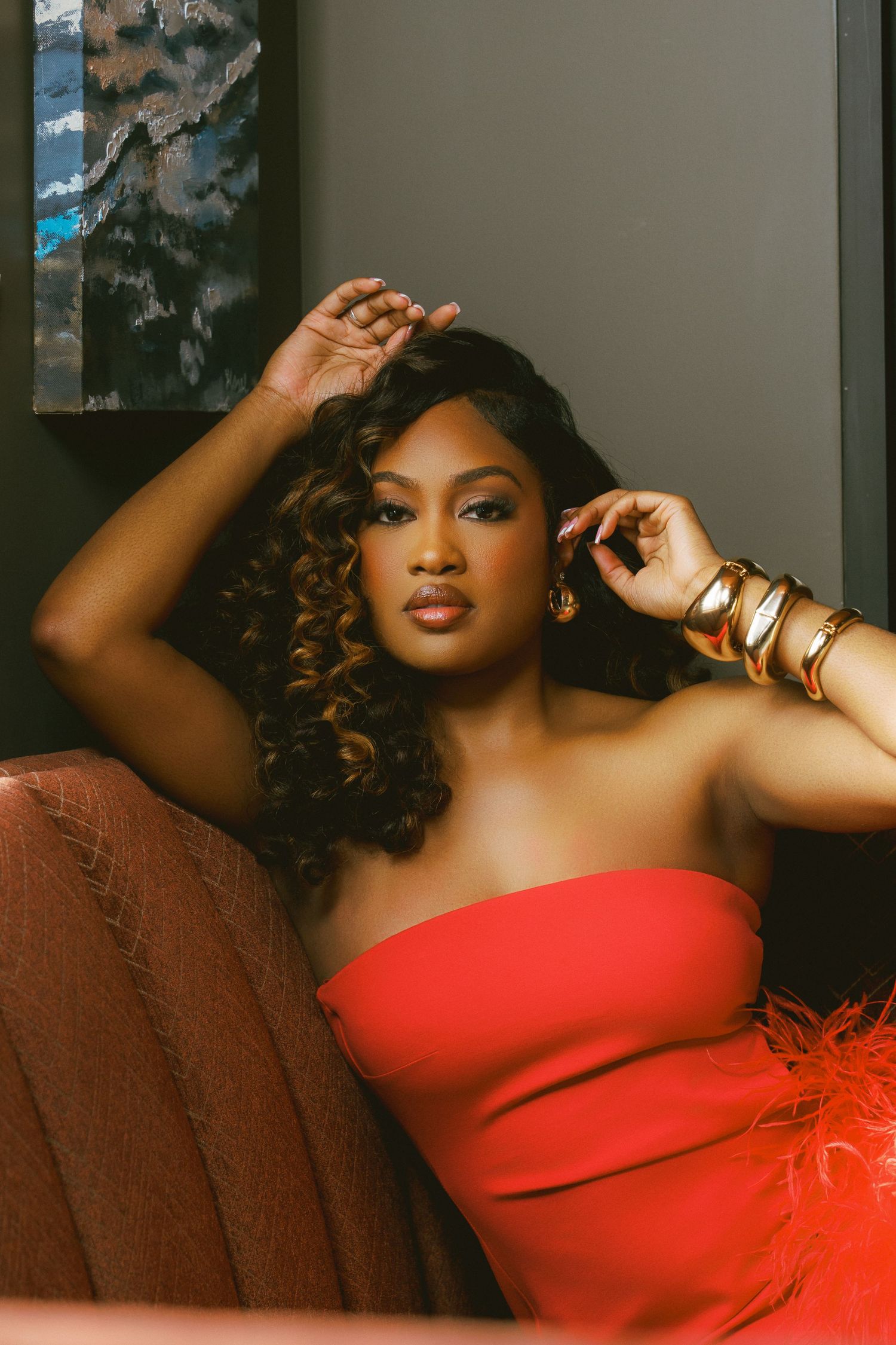 Fashion portrait of a model in a striking red strapless dress with feather details against a dark background.