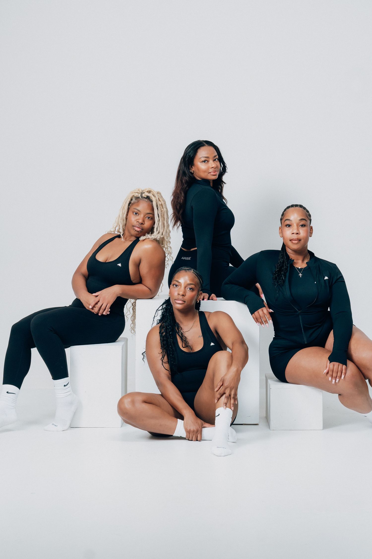 Group photo series with models in black outfits posing artistically on white blocks.