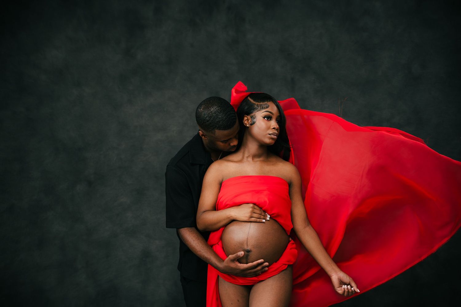 Maternity photography series in flowing red fabric against dark background.