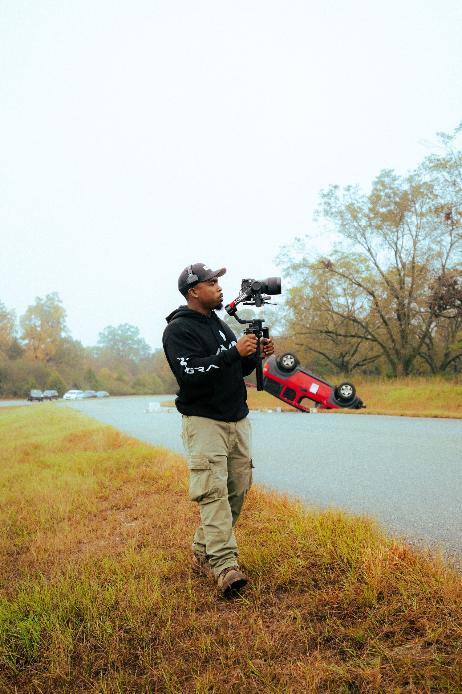 Photographer capturing footage outdoors with professional camera equipment on grassy hill.