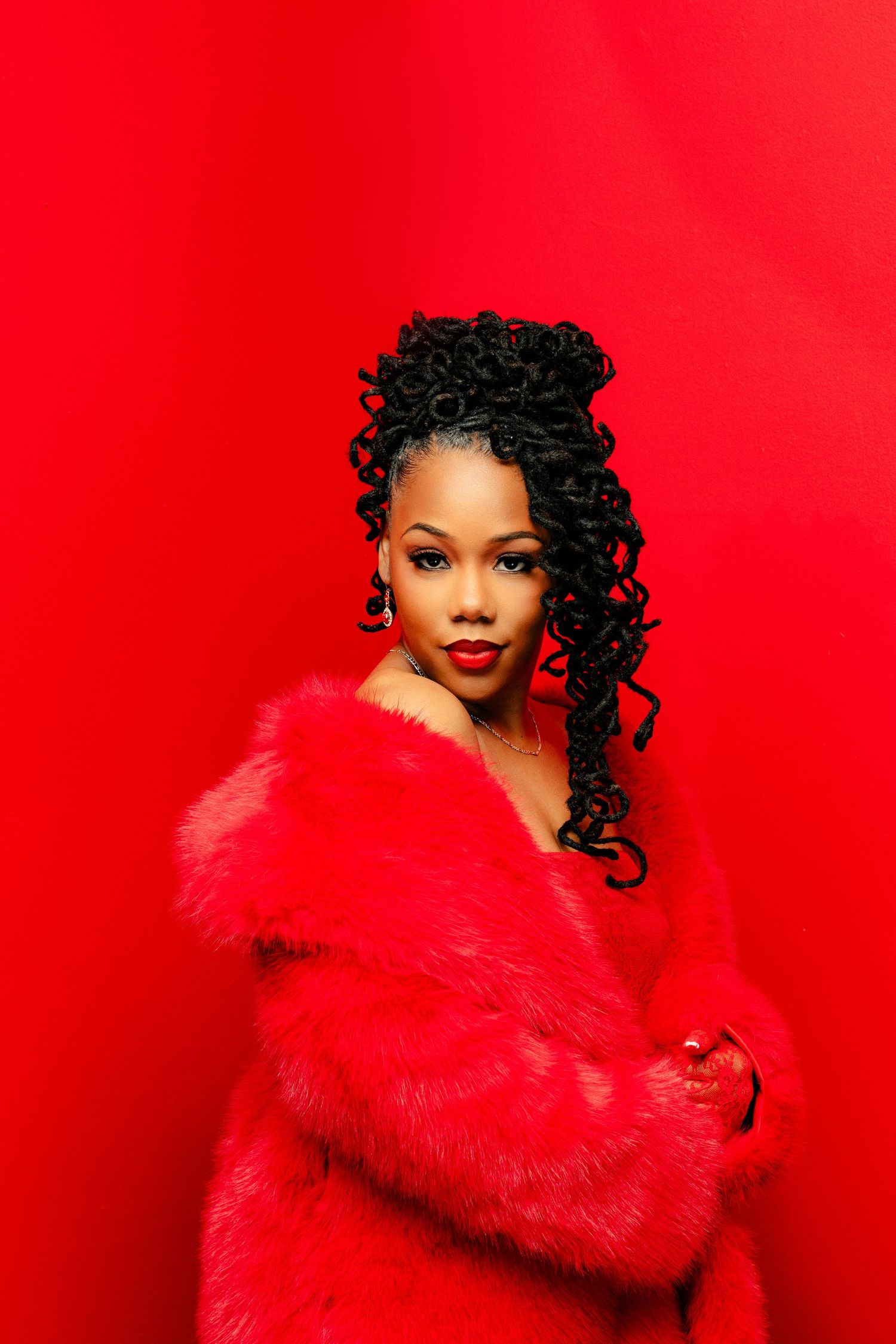 Fashion portrait against vibrant red background featuring dramatic fur stole and curly hair styling.
