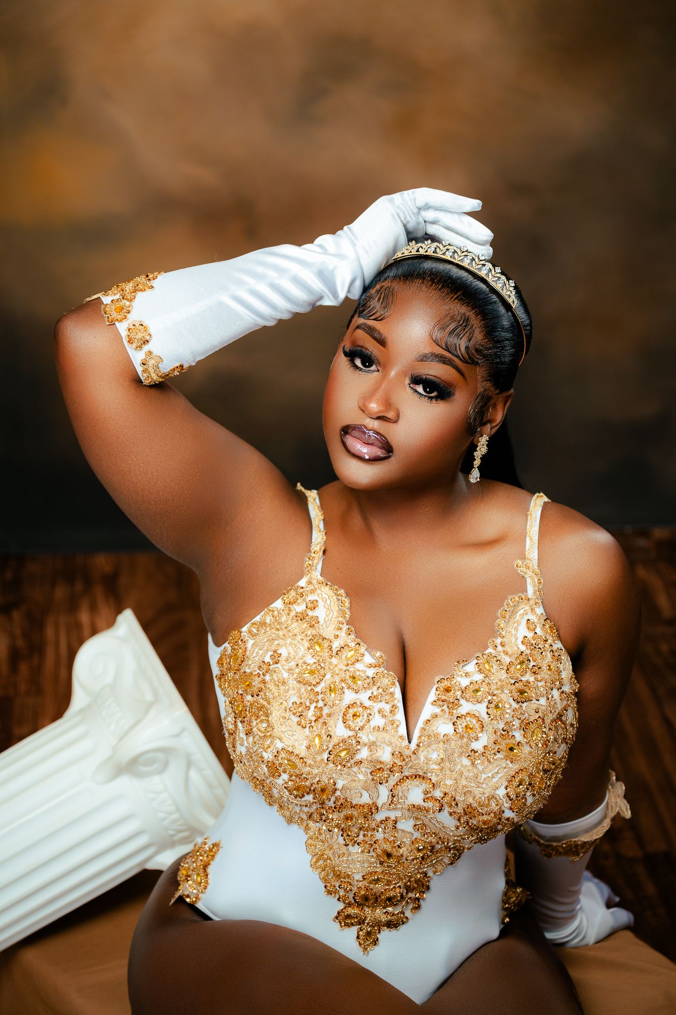 Glamorous portrait in white and gold embellished bodysuit with matching gloves and crown.