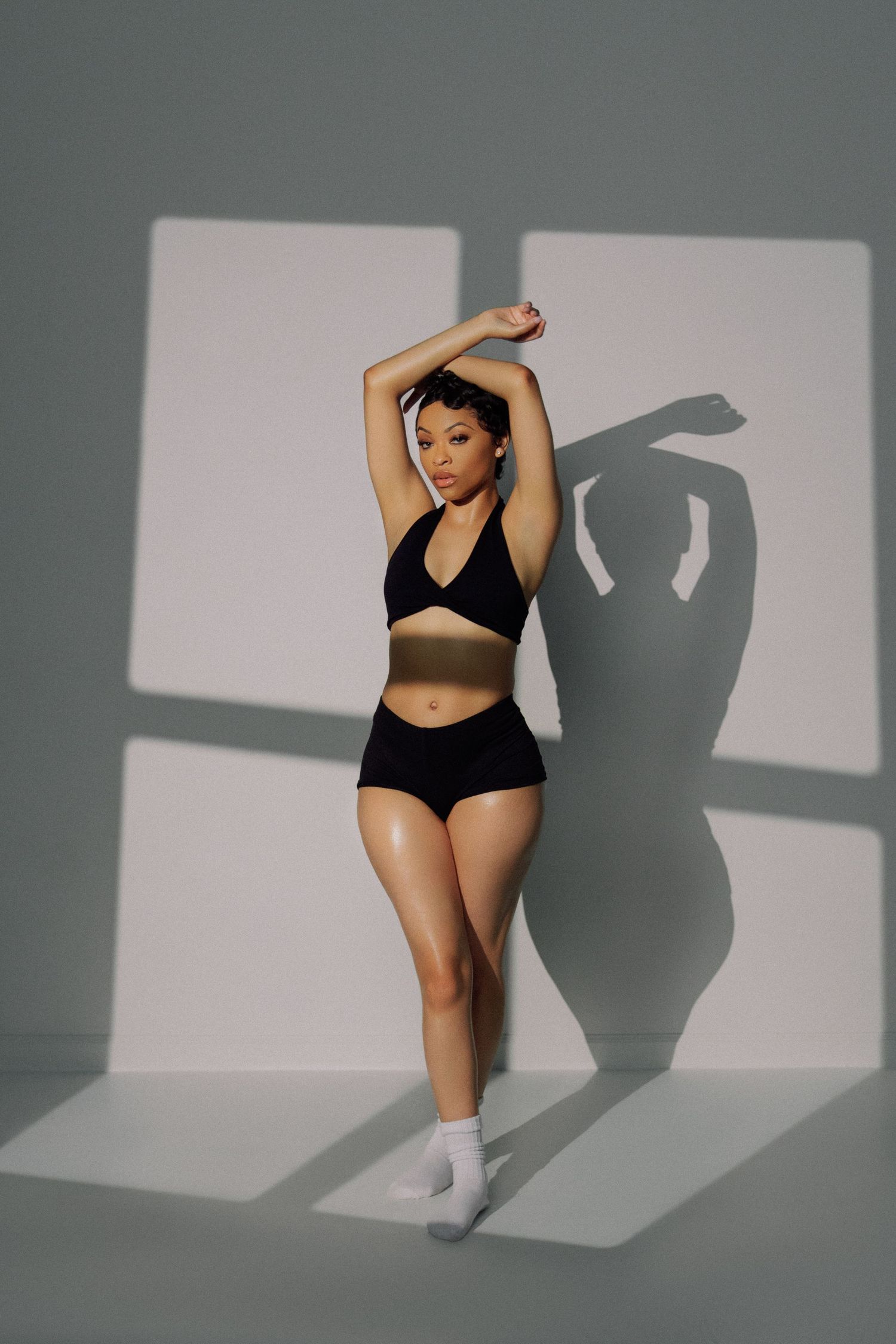 Model in black athletic wear poses against grey backdrop creating dramatic shadows.