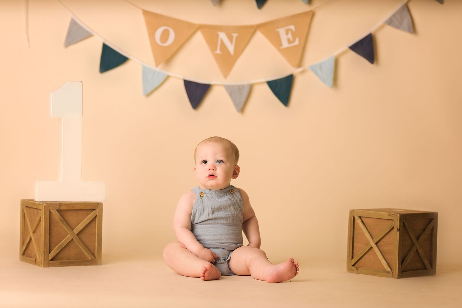 Baby sitting on beige backdrop with wooden boxes and triangle banner decoration.