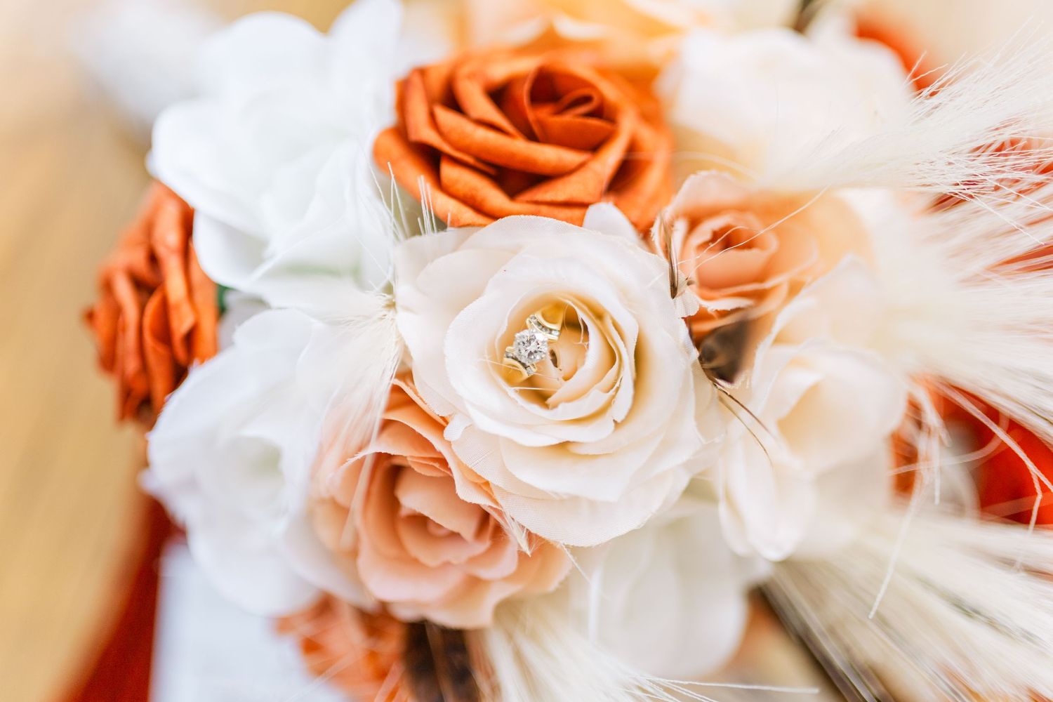 Close-up of orange and white wedding bouquet with roses and feather accents.