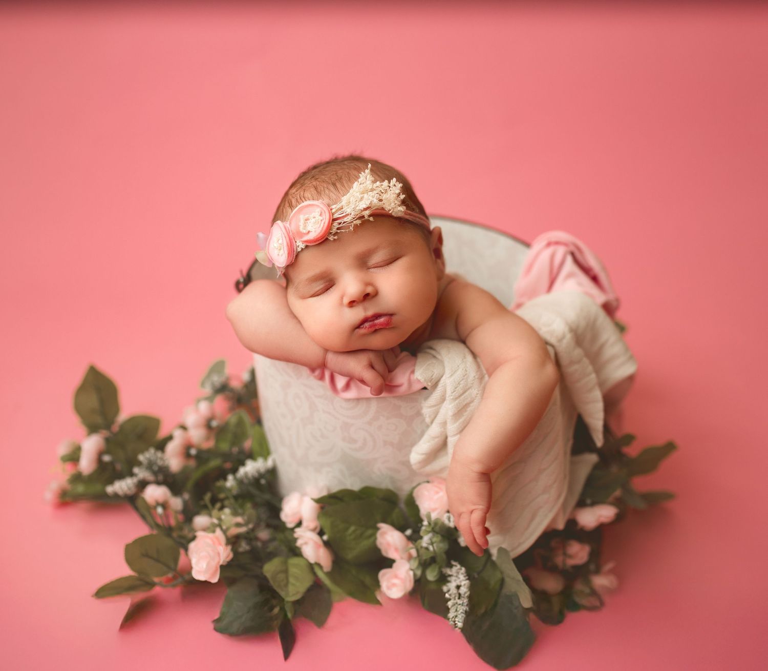 Newborn baby sleeping among roses wearing delicate floral headband.