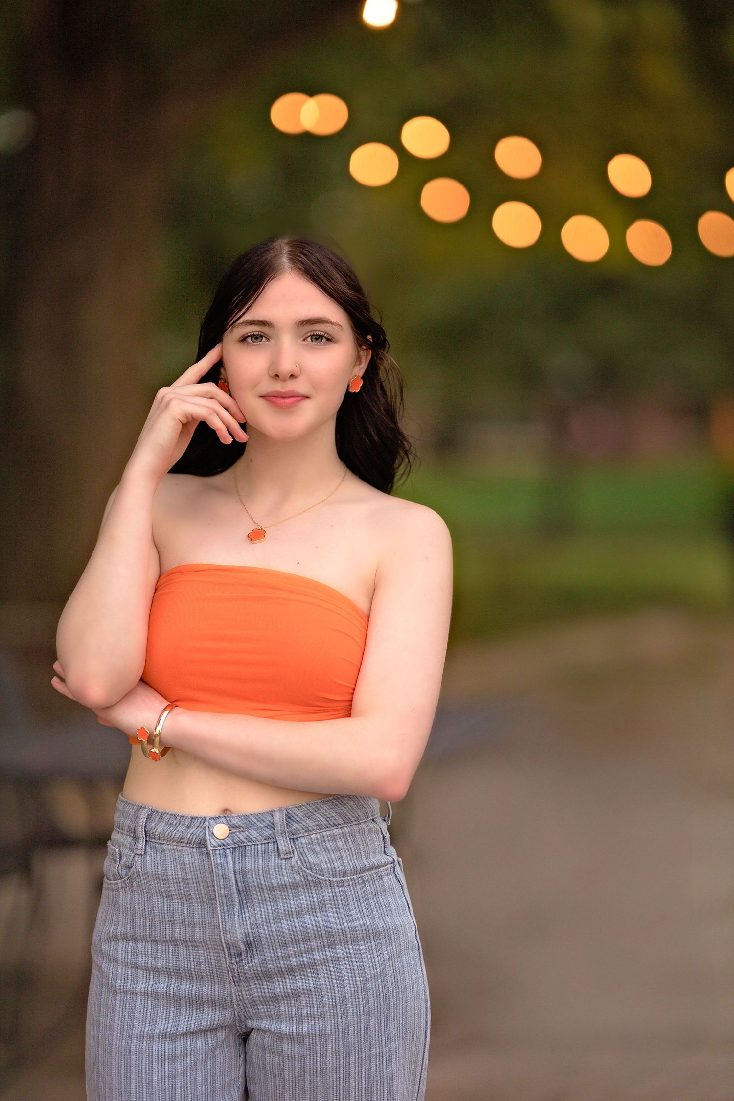 Evening portrait with bokeh lights showing casual summer style with orange top and striped pants.