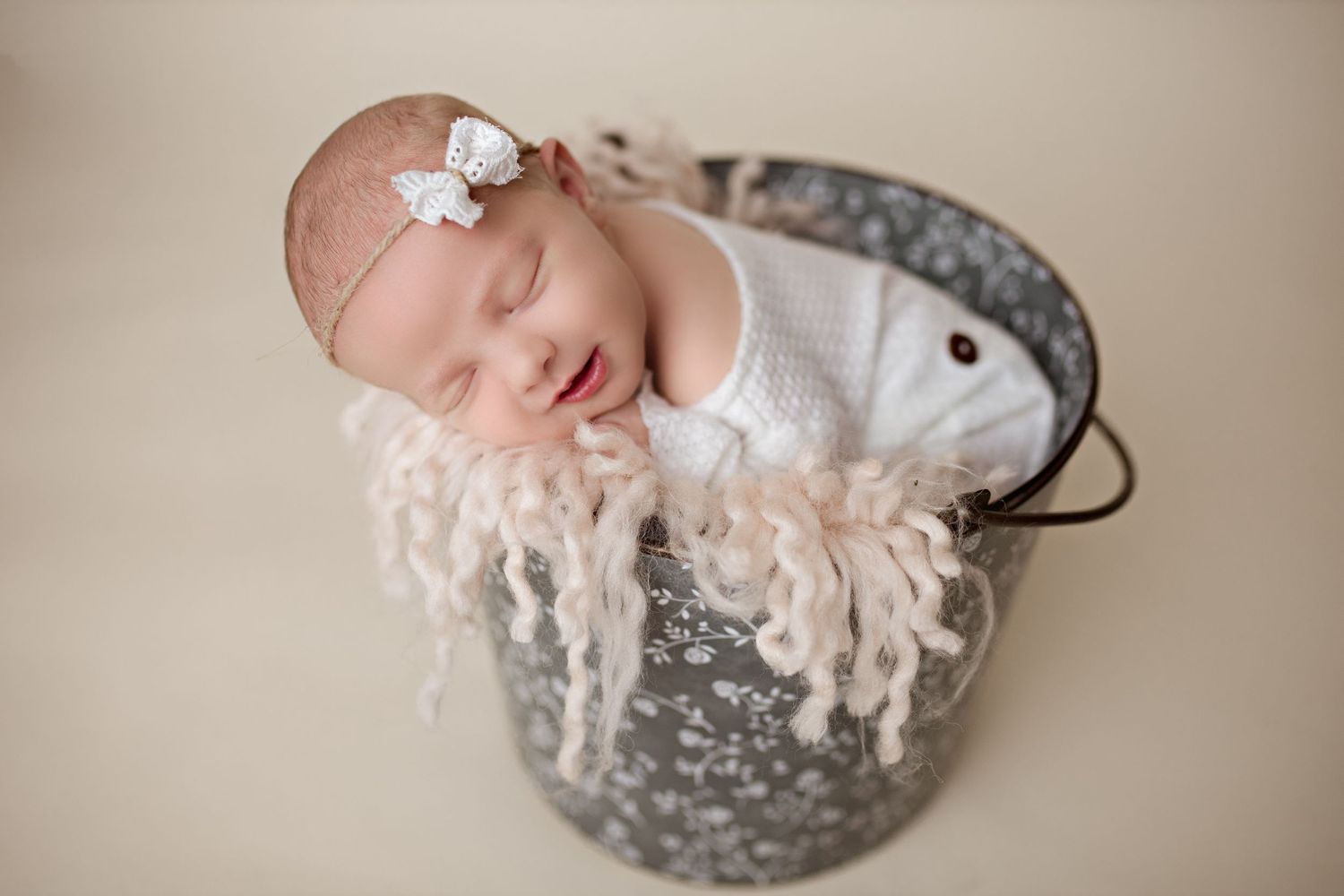 Sleeping newborn with delicate headband posed in rustic metal bucket with cream padding.