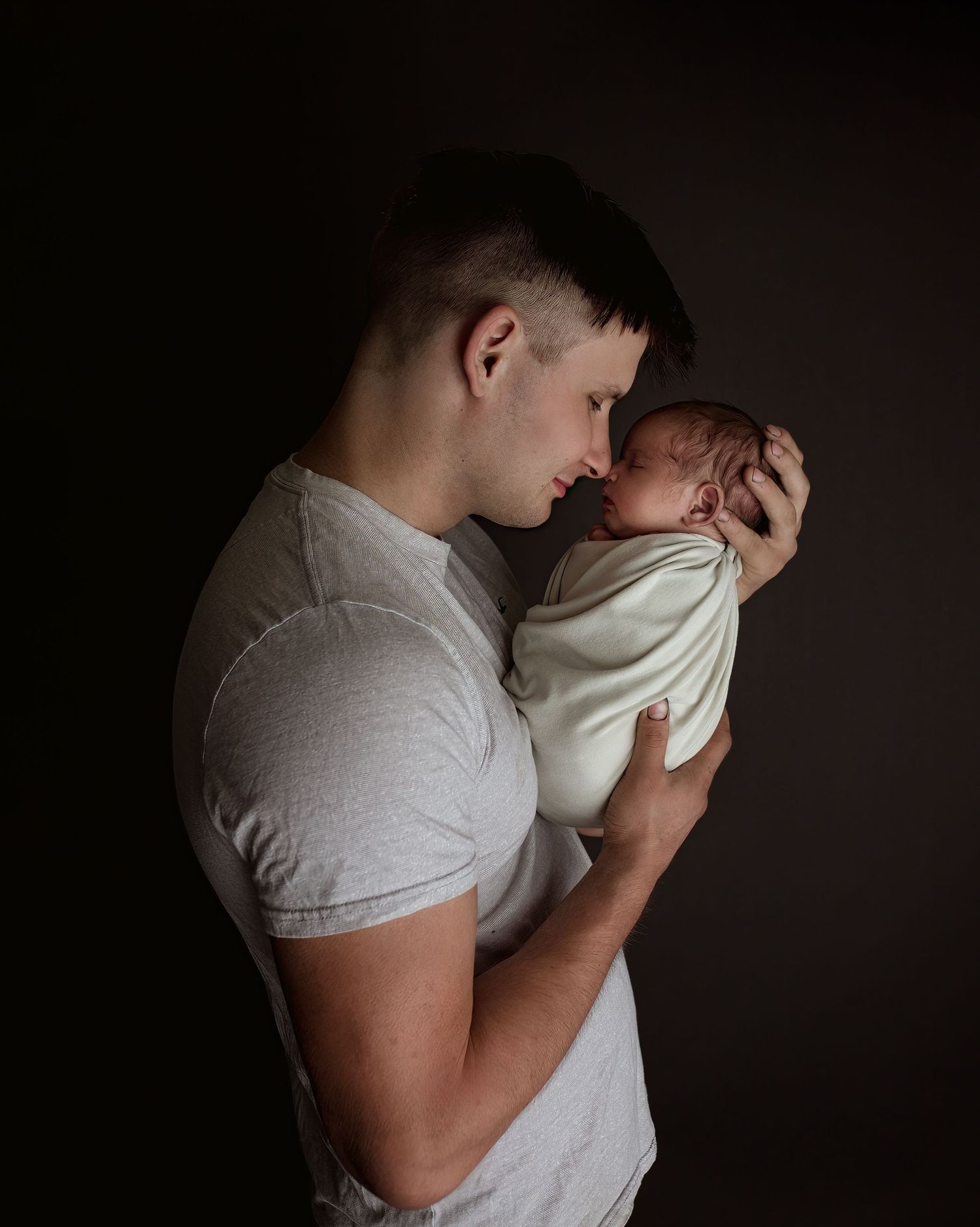 Tender moment captured in moody lighting as parent holds sleeping newborn.