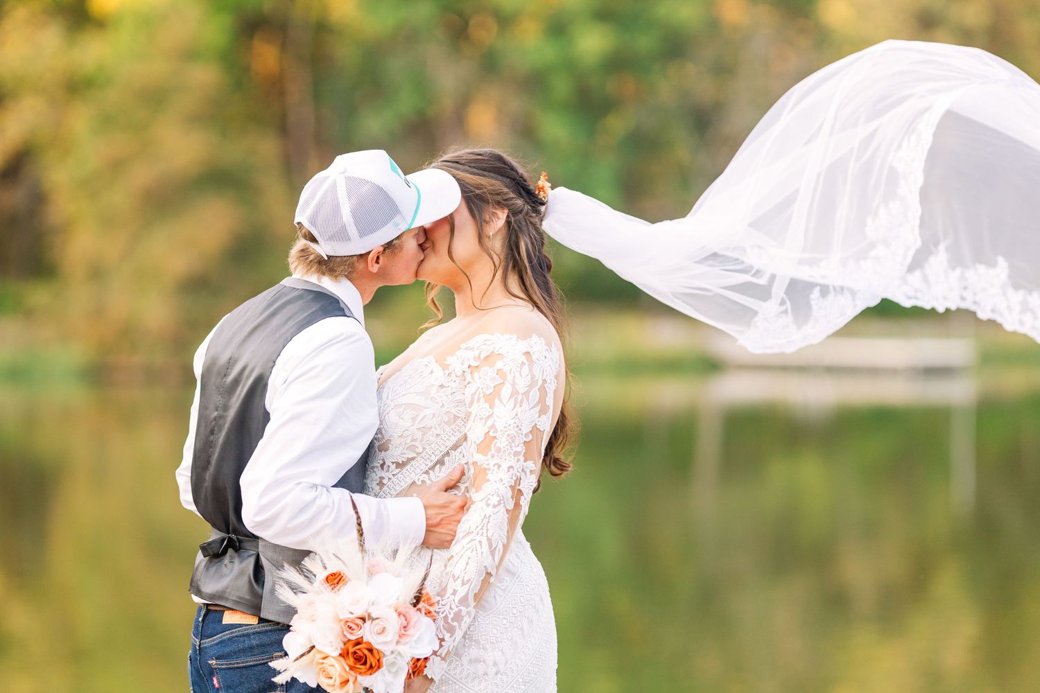 Wedding photo with flowing veil against lake backdrop.