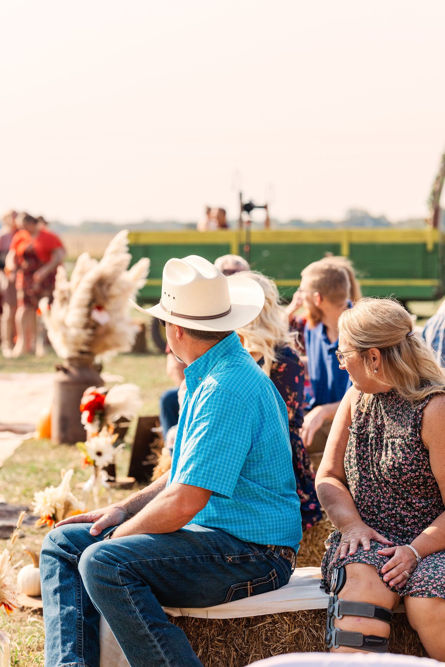 Wedding guests seated on hay bales at an outdoor country celebration.