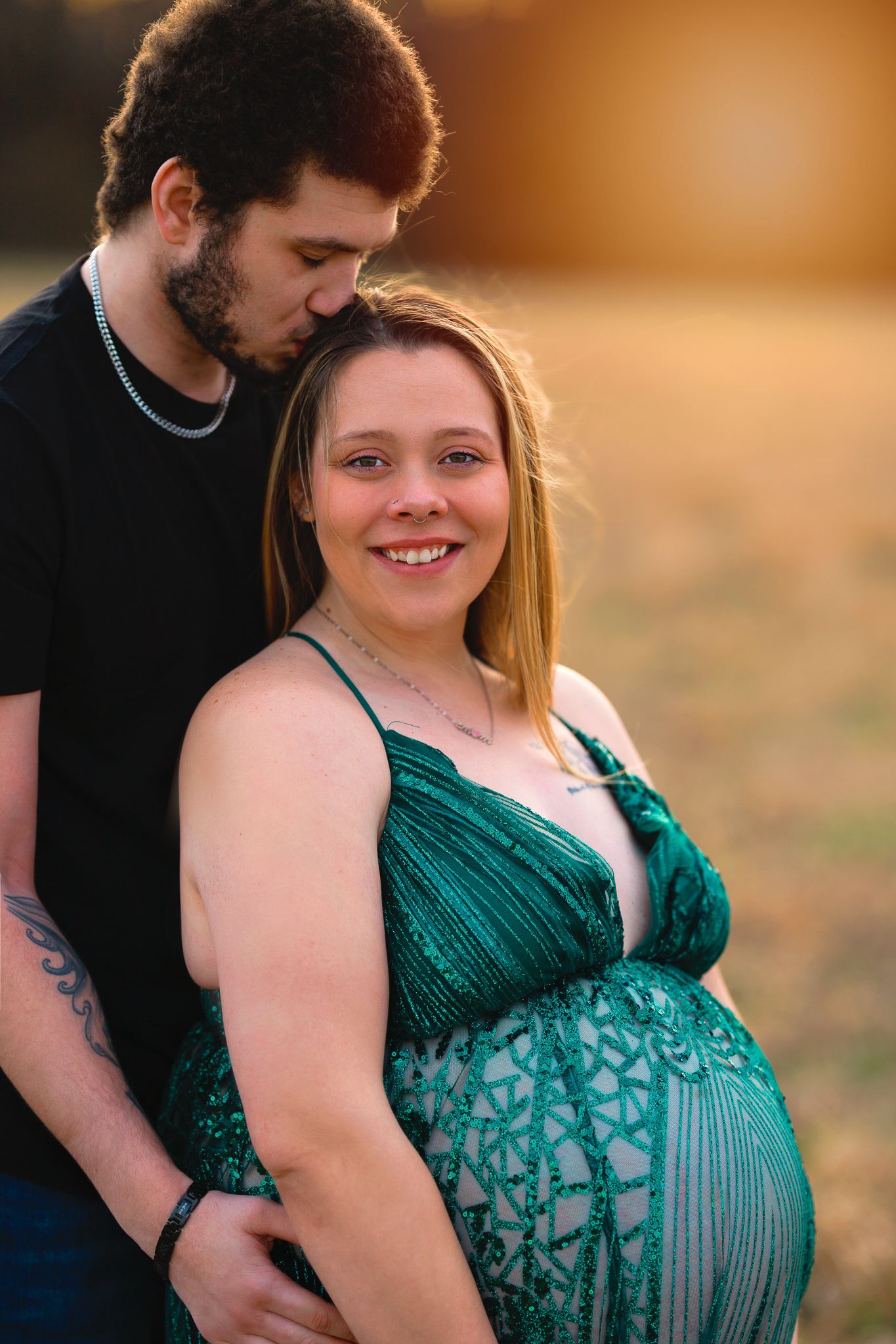 A maternity portrait featuring a couple embracing during sunset, with the woman wearing a green dress.