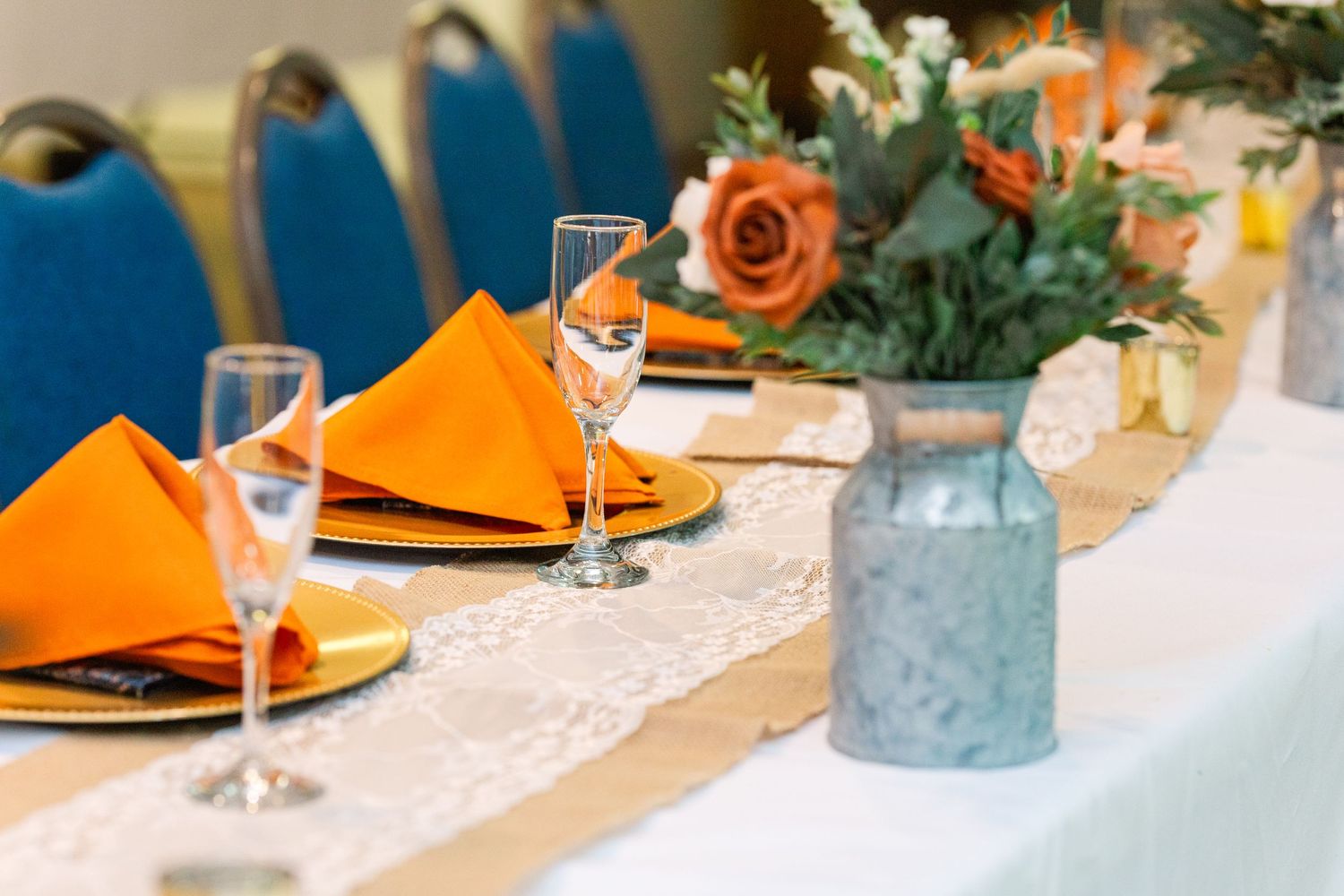 Wedding reception table set with orange napkins, wine glasses and floral centerpieces.