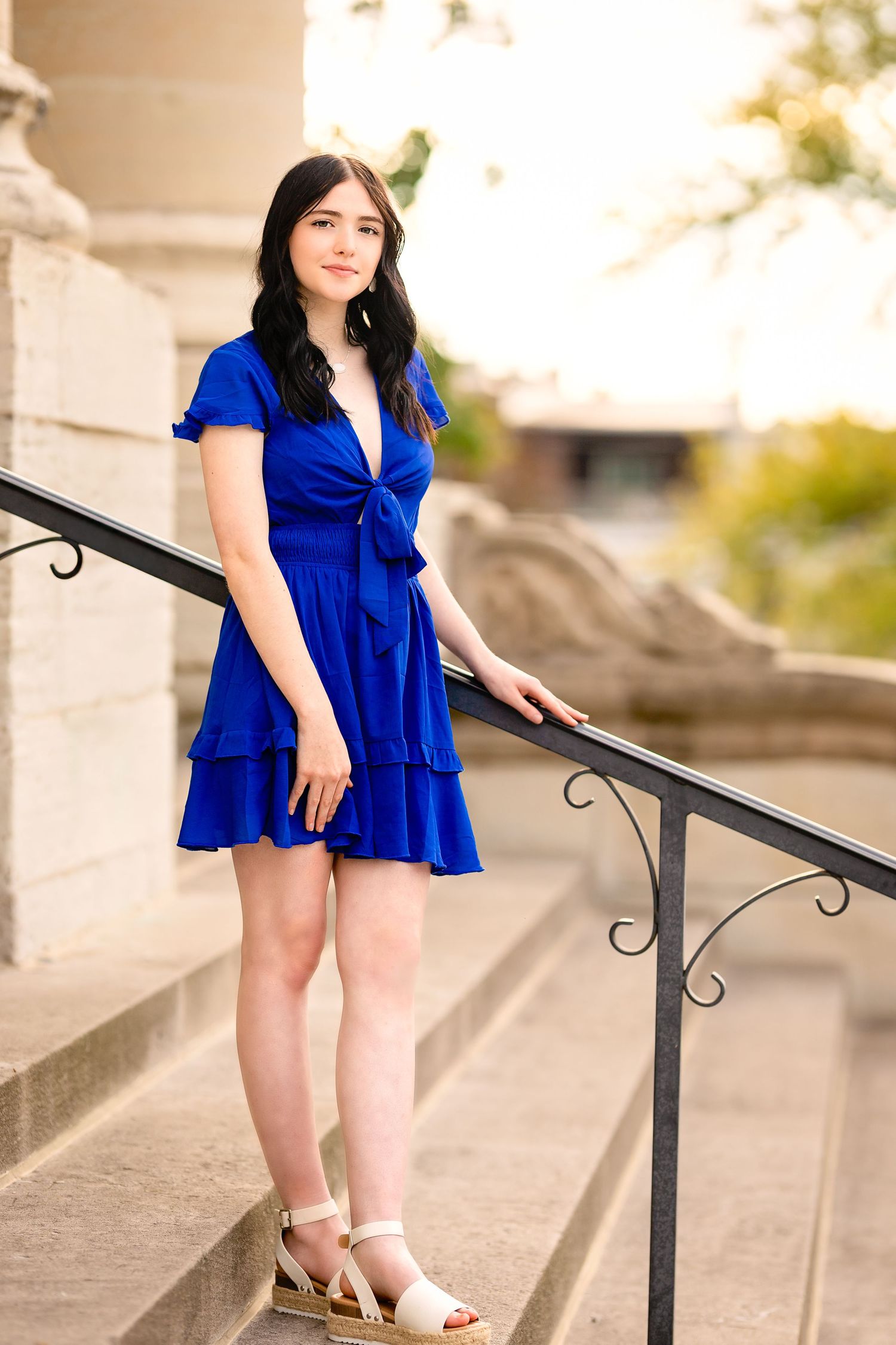 Young woman in royal blue dress poses on stone steps at sunset.