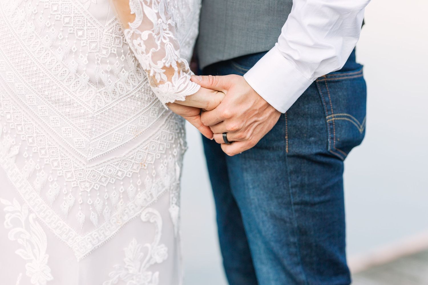 Close-up detail of hands and lace wedding dress against denim.