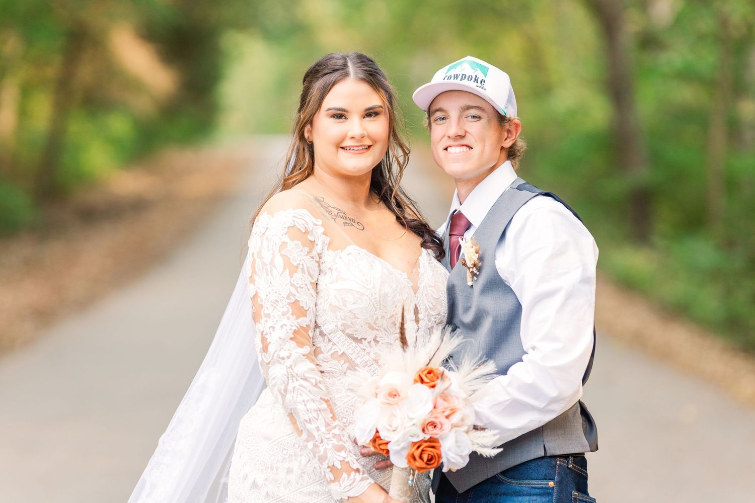 Wedding couple sharing a joyful moment outdoors on a tree-lined path.