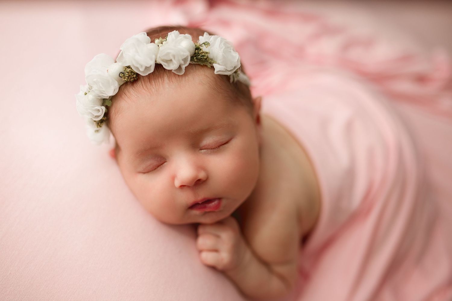 Sleeping newborn with white flower crown on pink background.