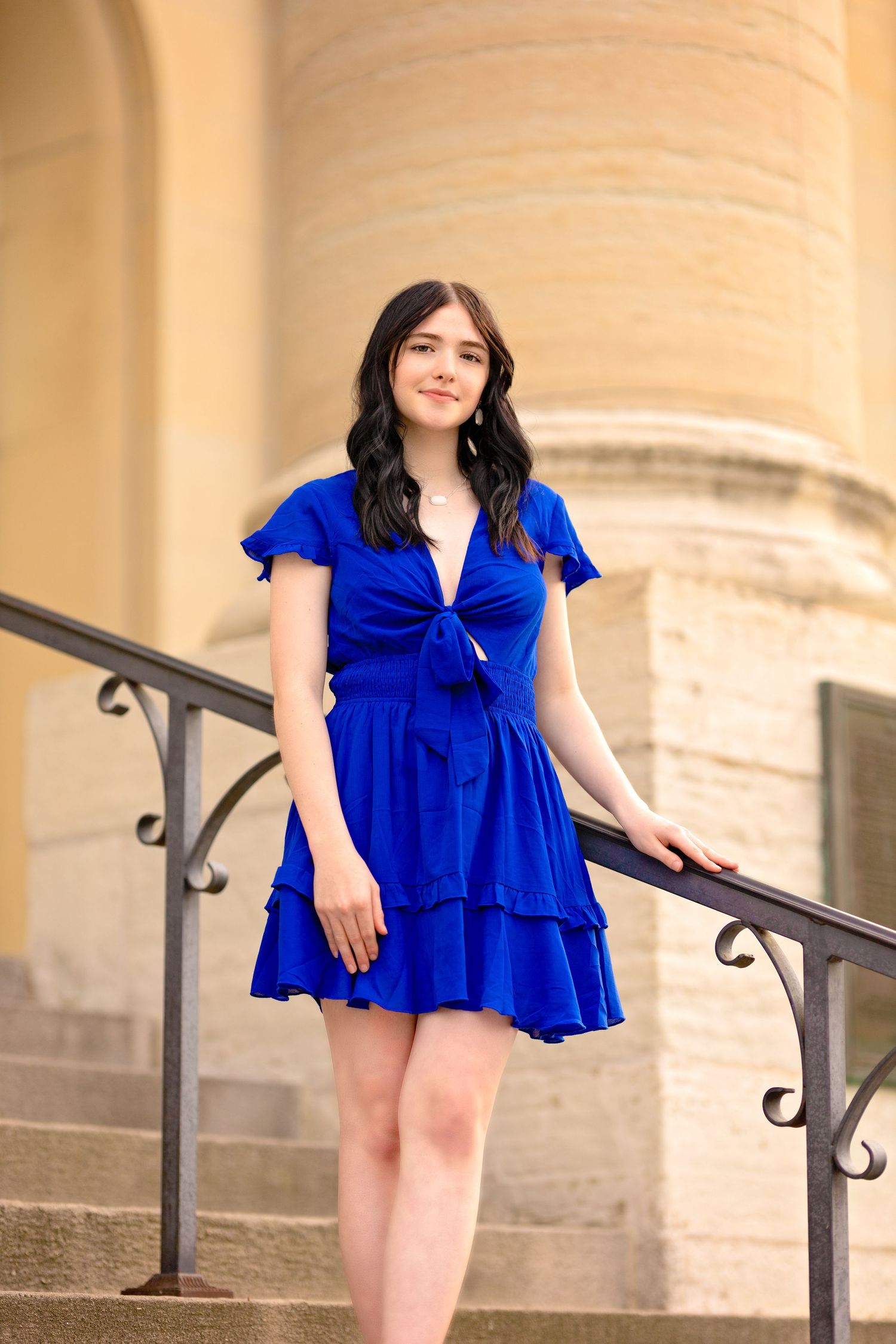 A portrait on stone steps features a vibrant royal blue ruffle dress and architectural columns.