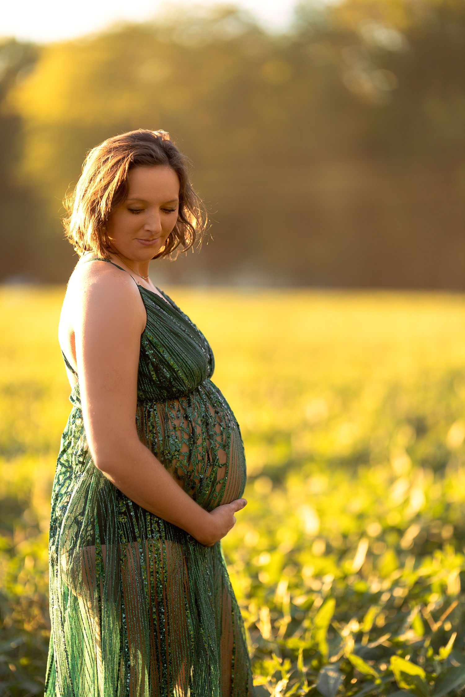Glowing sunset maternity portrait in a green sequined dress amid wildflowers.