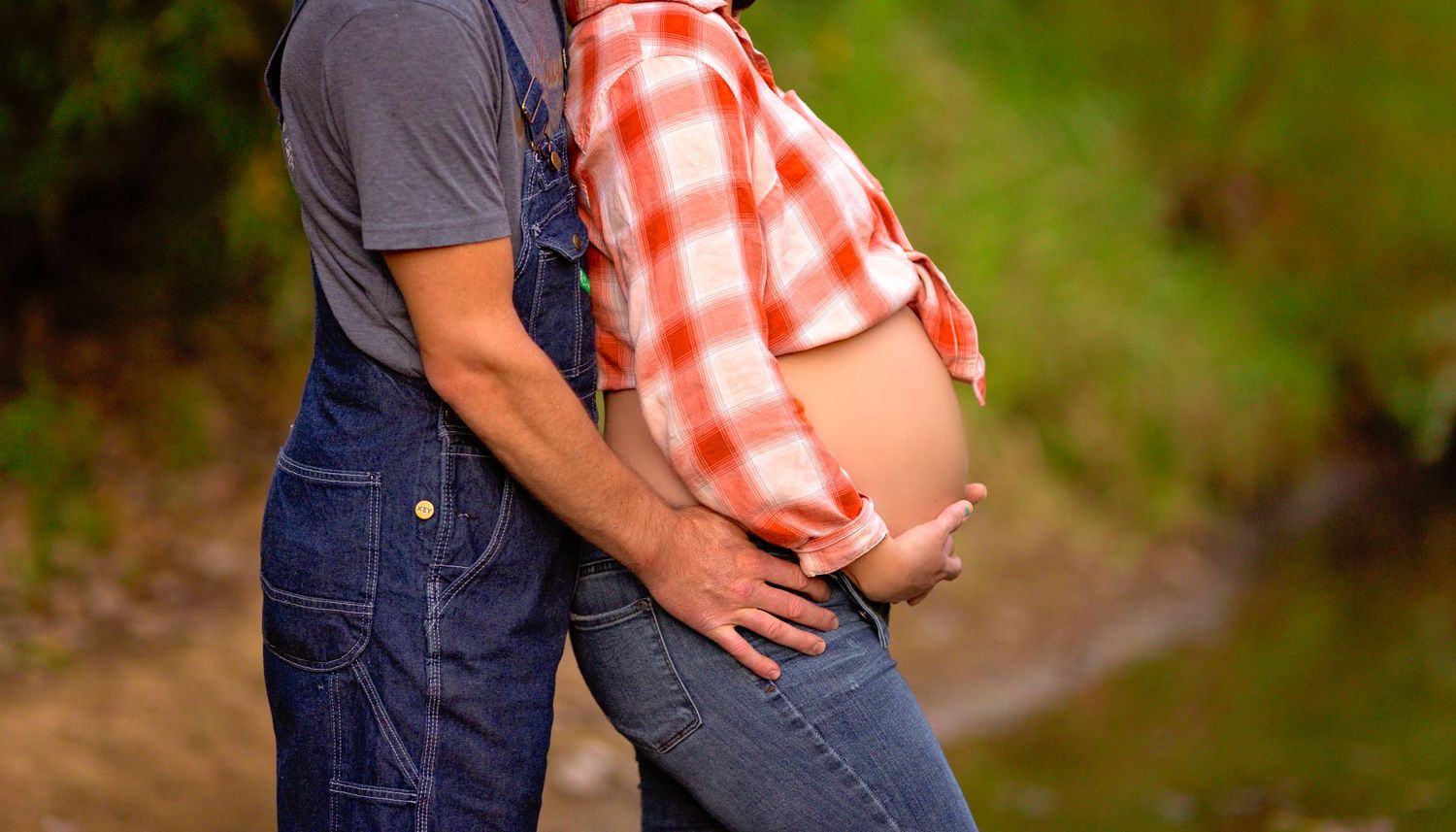 Intimate maternity photo with hands cradling pregnant belly in plaid shirt.