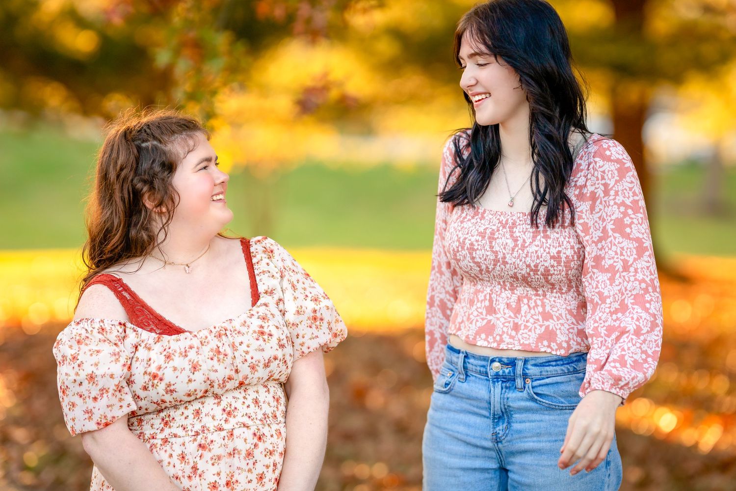 Two people in matching floral tops share a candid moment amid golden fall foliage.