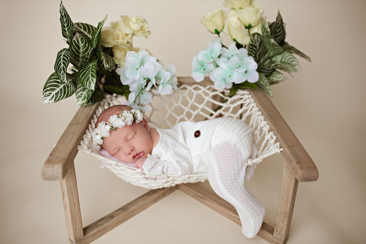 Sleeping infant on rustic wooden chair with delicate floral arrangements.