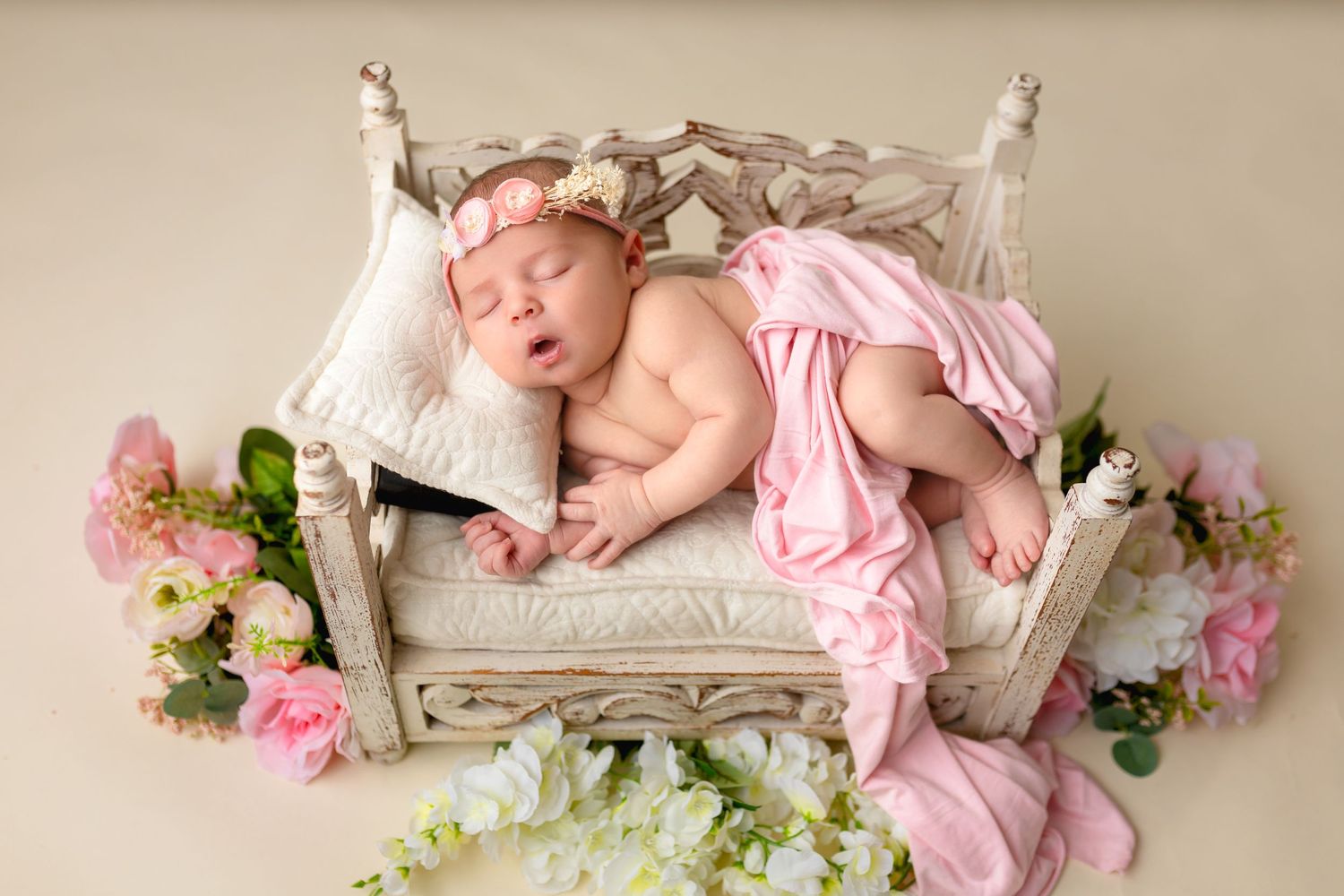 Sleeping baby on vintage bed prop with pink fabric and floral decorations.